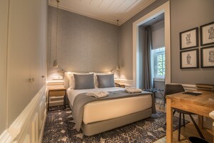 Un dormitorio con cama, mesitas de noche, un escritorio y una ventana.
