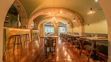 A restaurant with wooden tables and chairs, arched brick ceilings, and hanging pendant lights.