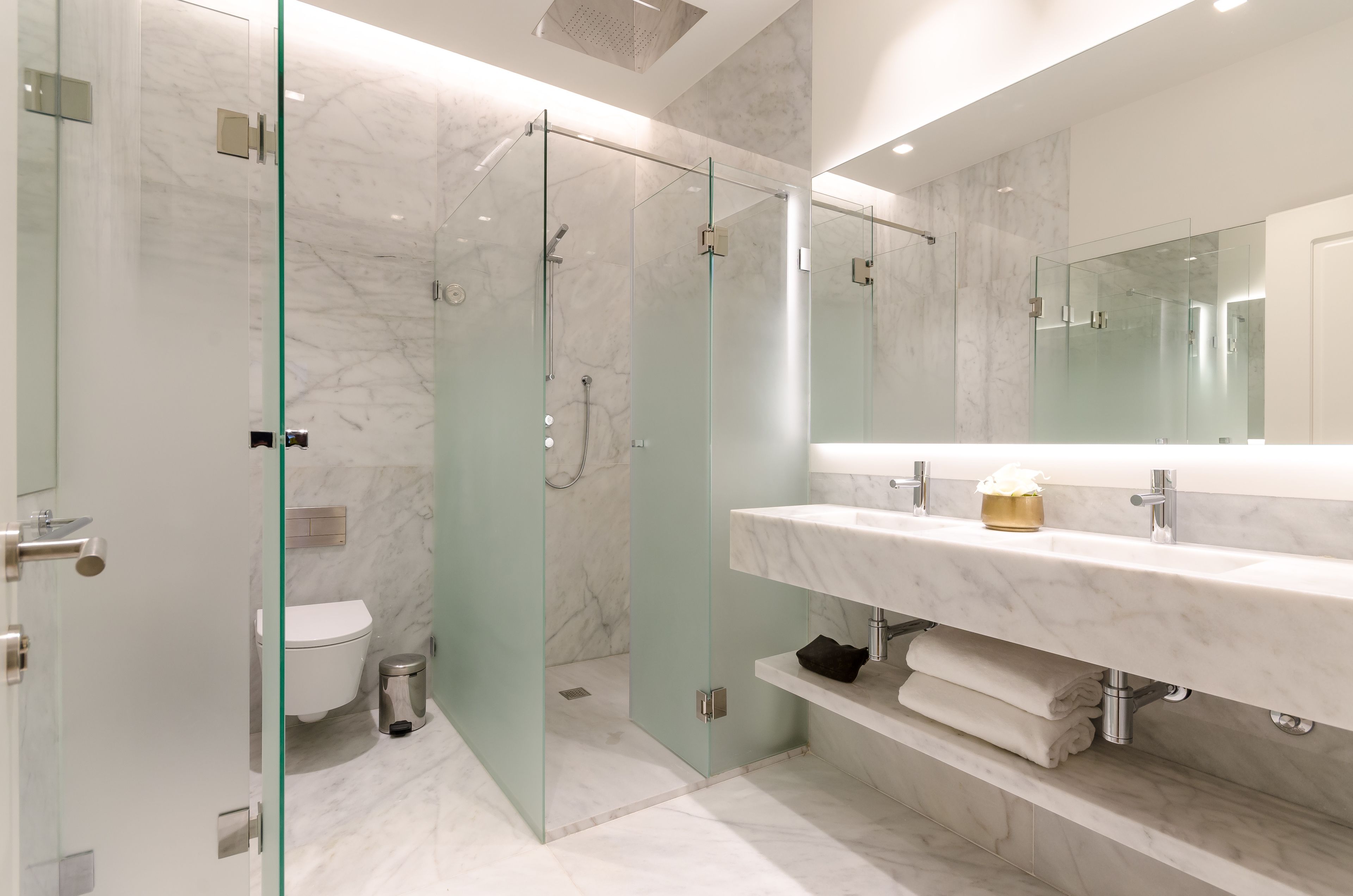 A modern bathroom with a glass-enclosed shower, a marble sink, and a large mirror.