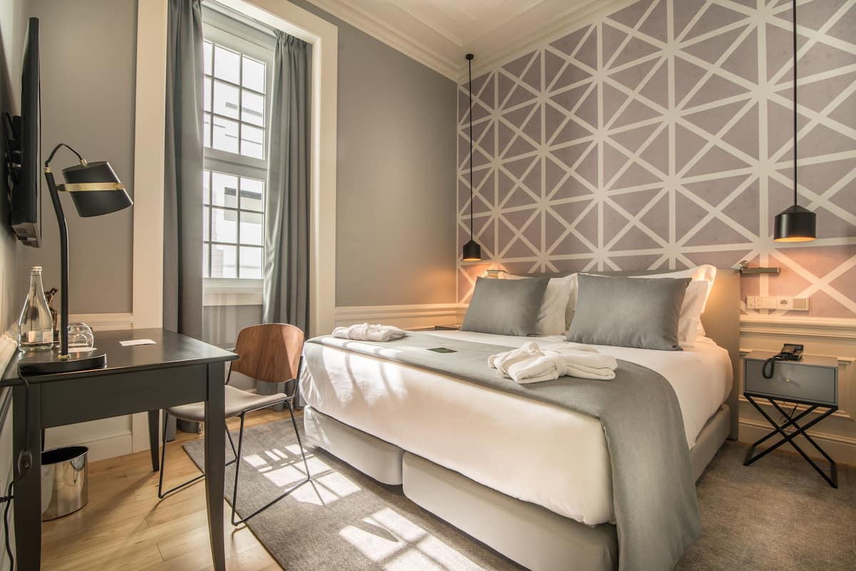 Una habitación de hotel moderna con una cama grande, un escritorio, una silla y una mesita de noche.