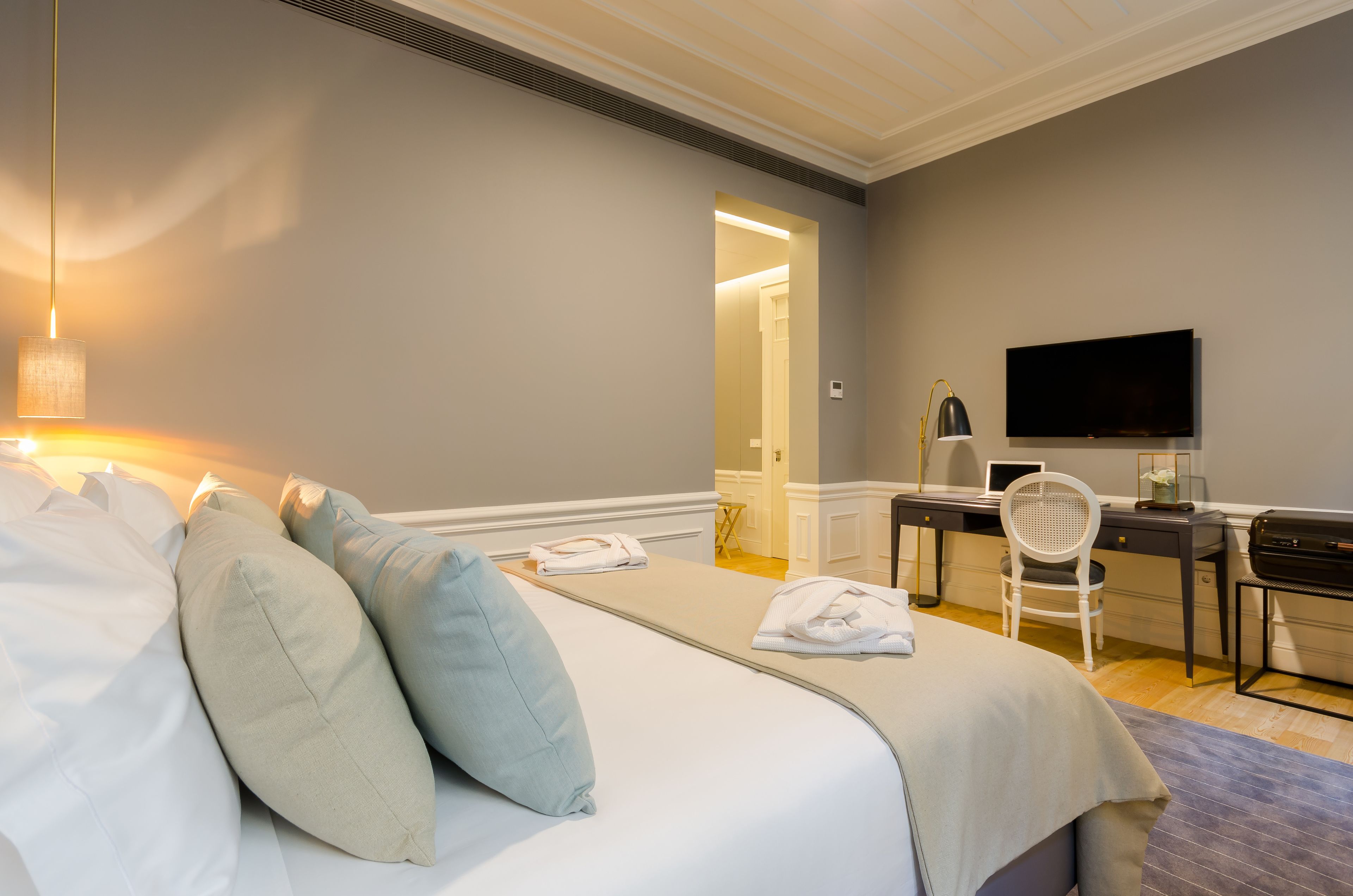 Quarto de hotel com cama, escrivaninha, cadeira, televisão e luminária.