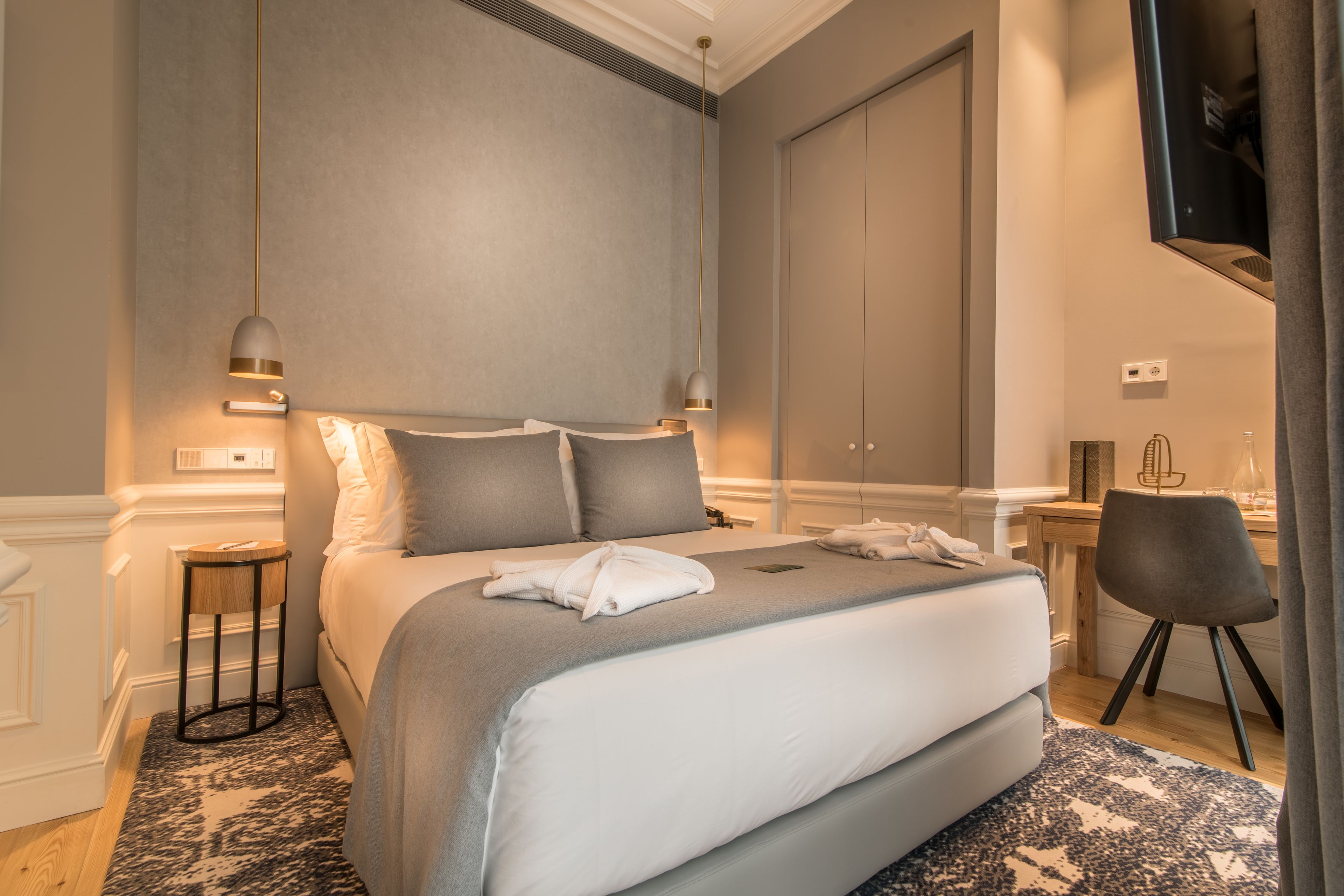A modern hotel room with a large bed, bedside tables, a desk, and a television.