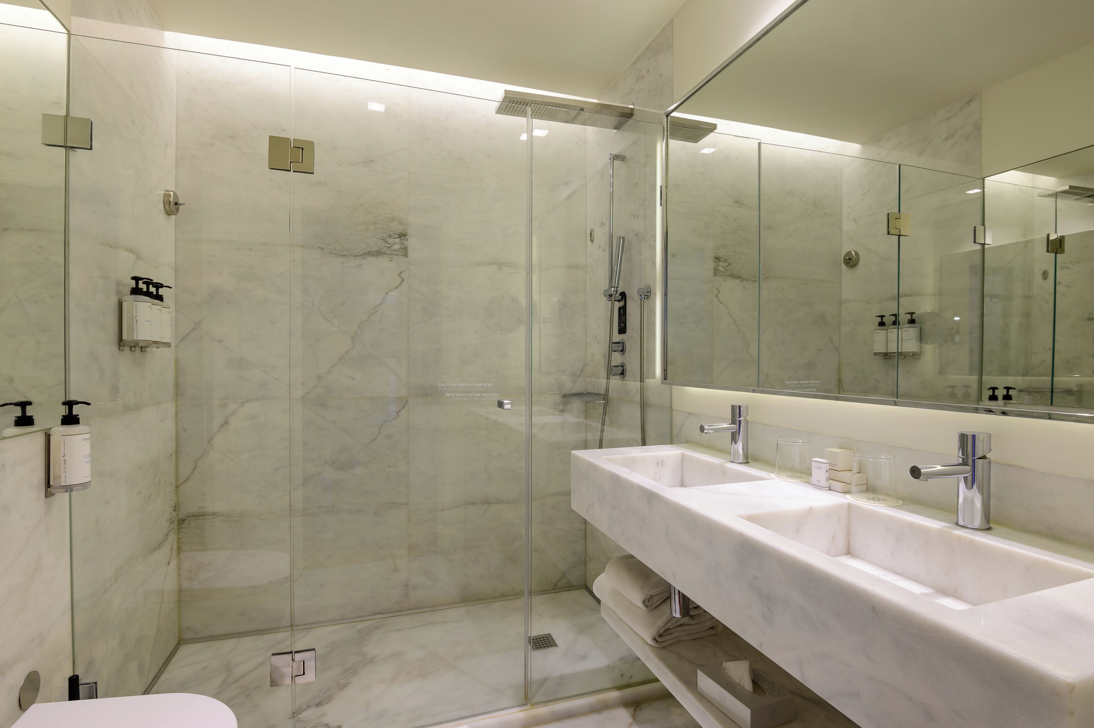 A modern bathroom with a glass-enclosed shower, a large mirror, and a white marble sink.