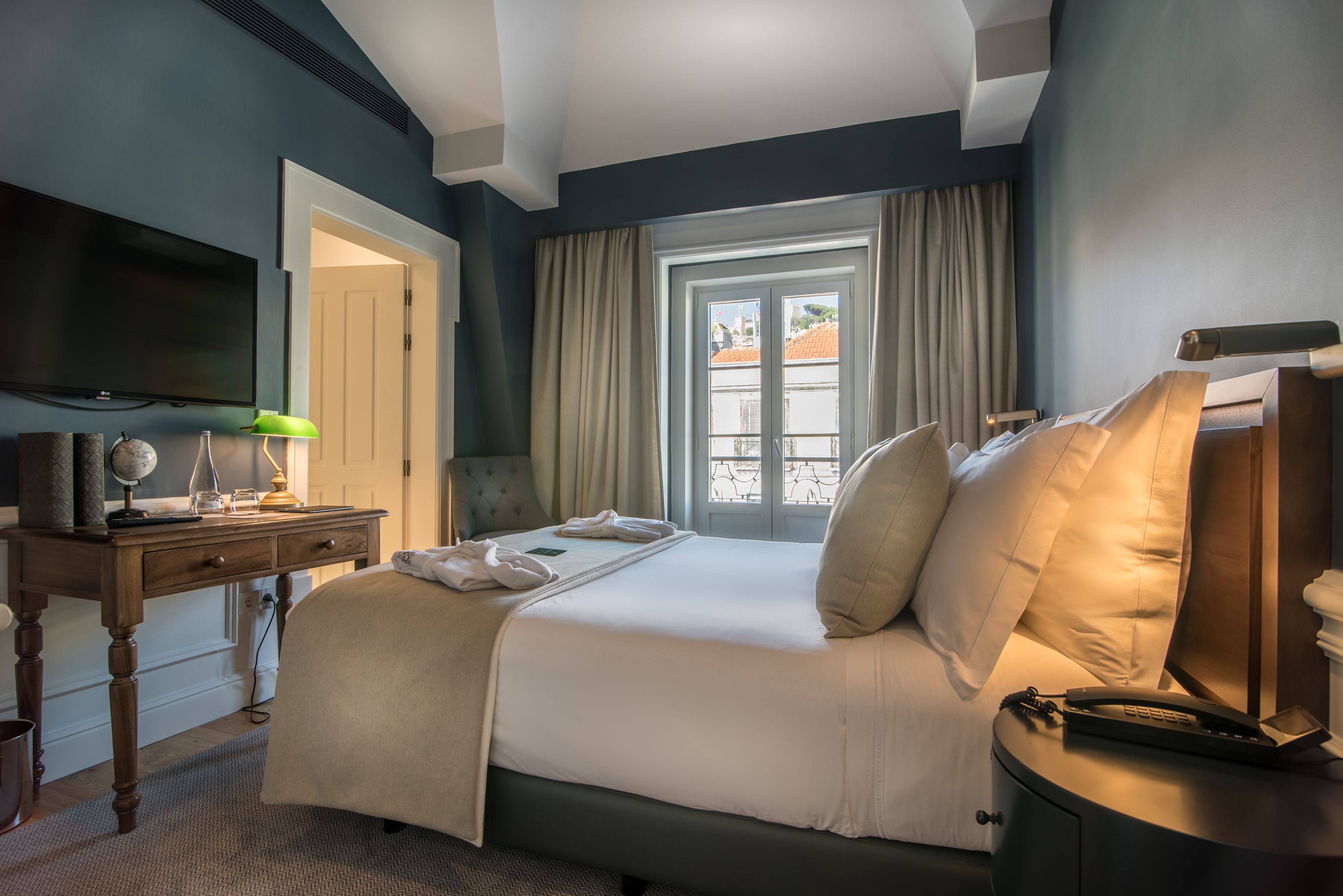 A hotel room with a bed, a desk, a television, and a window with curtains.