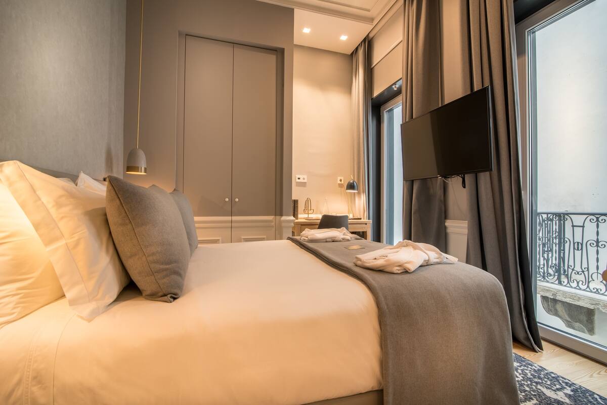 Habitación de hotel con una cama grande, un televisor de pantalla plana en la pared, un escritorio con lámpara y vistas al balcón.