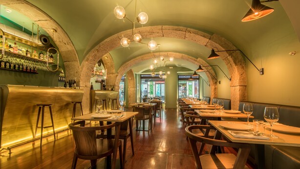 Ein Restaurant mit Holztischen und -stühlen, einem Barbereich mit Flaschen und gewölbten Decken.