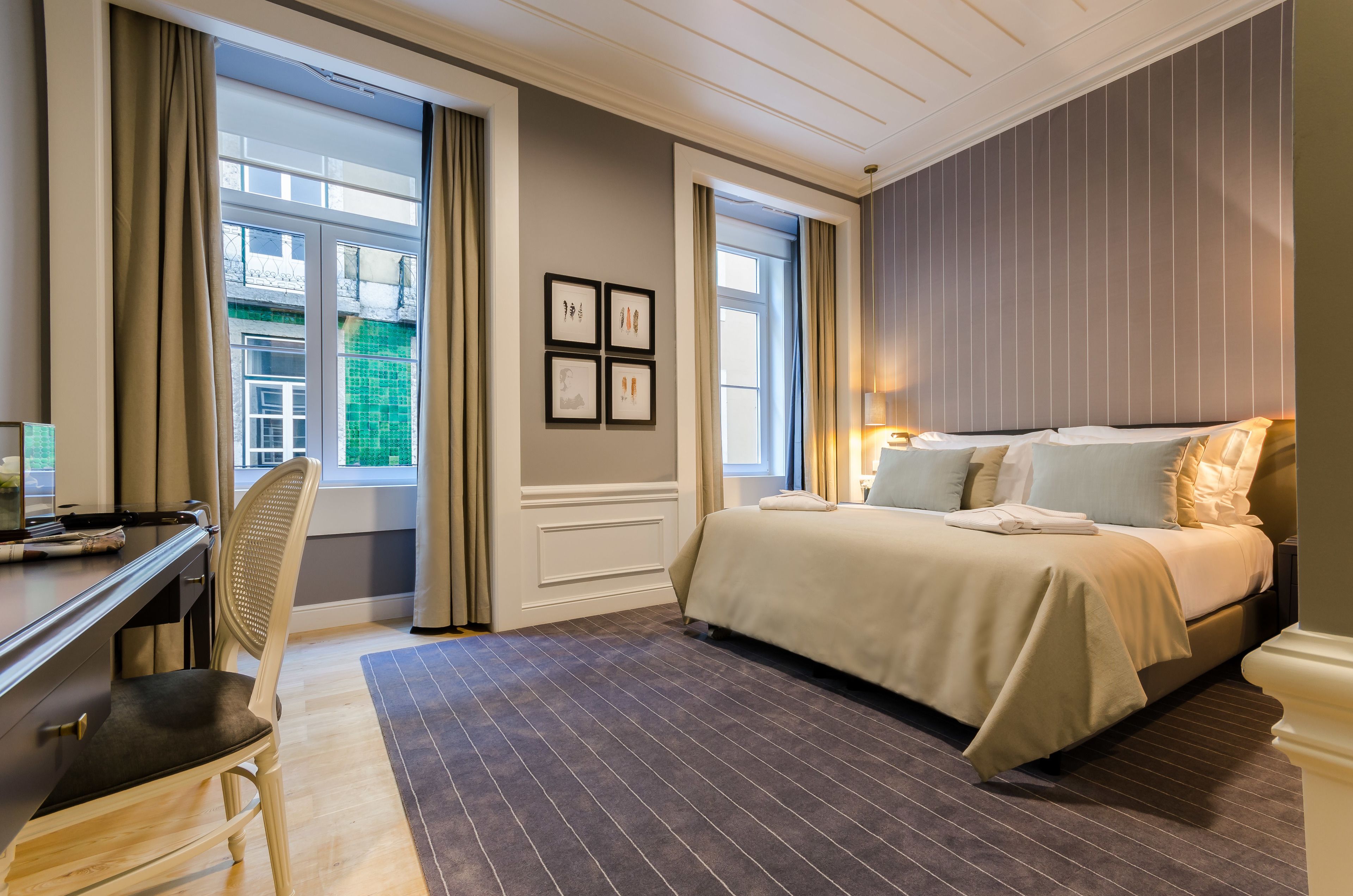 Et hotelværelse med seng, skrivebord, stol og store vinduer.