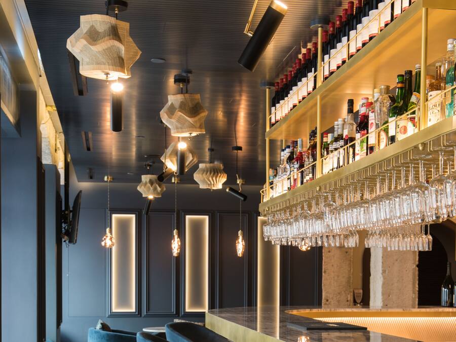 A bar area with a counter, bar stools, hanging light fixtures, and shelves stocked with bottles and glasses.