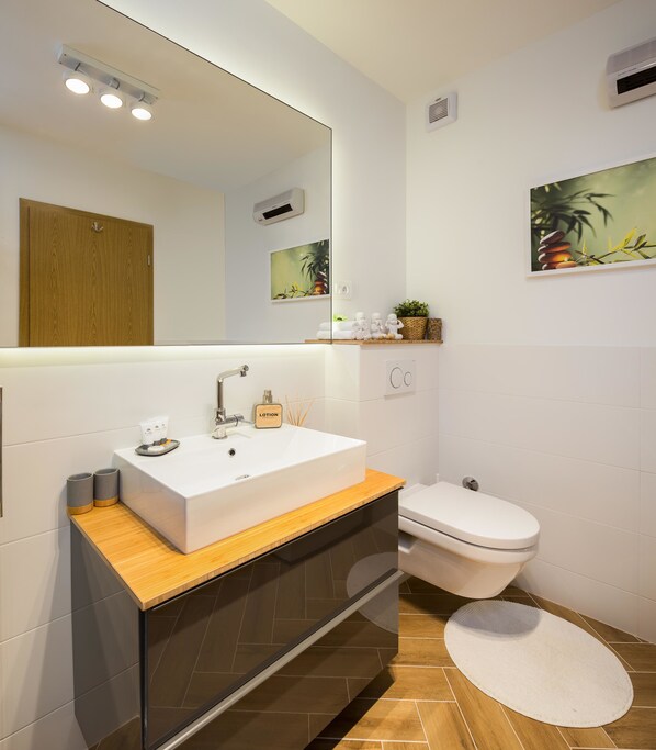 A modern bathroom with a white sink, a wooden vanity, a toilet, and a mirror. - Sun Spalato Views (Split)
