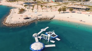 An aerial view of a coastal area with a sandy beach, a rocky breakwater, and a floating structure with multiple levels and a central dome. - Sun Spalato Views (Split)