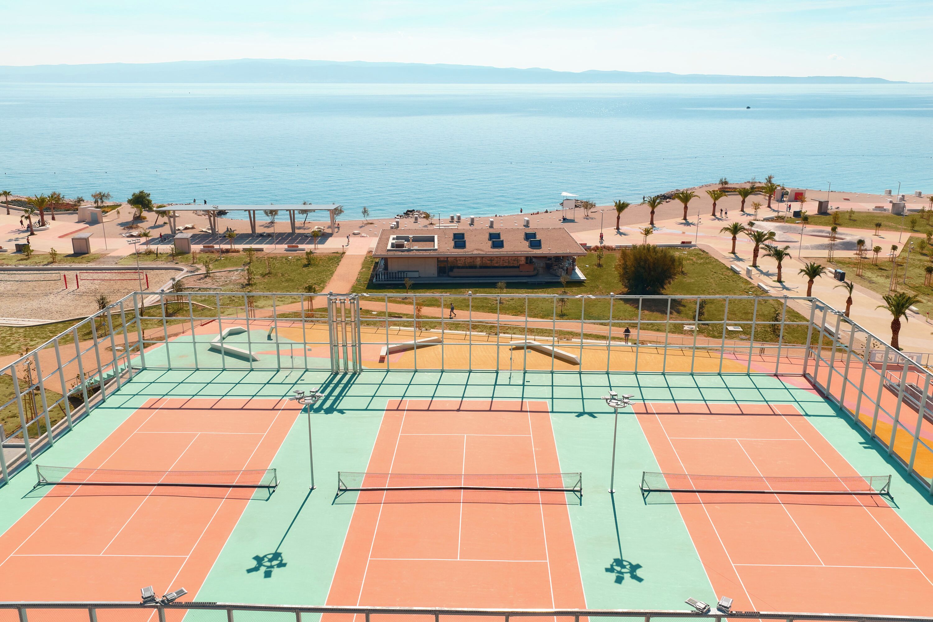 An outdoor tennis court with a view of the sea and a building in the background.