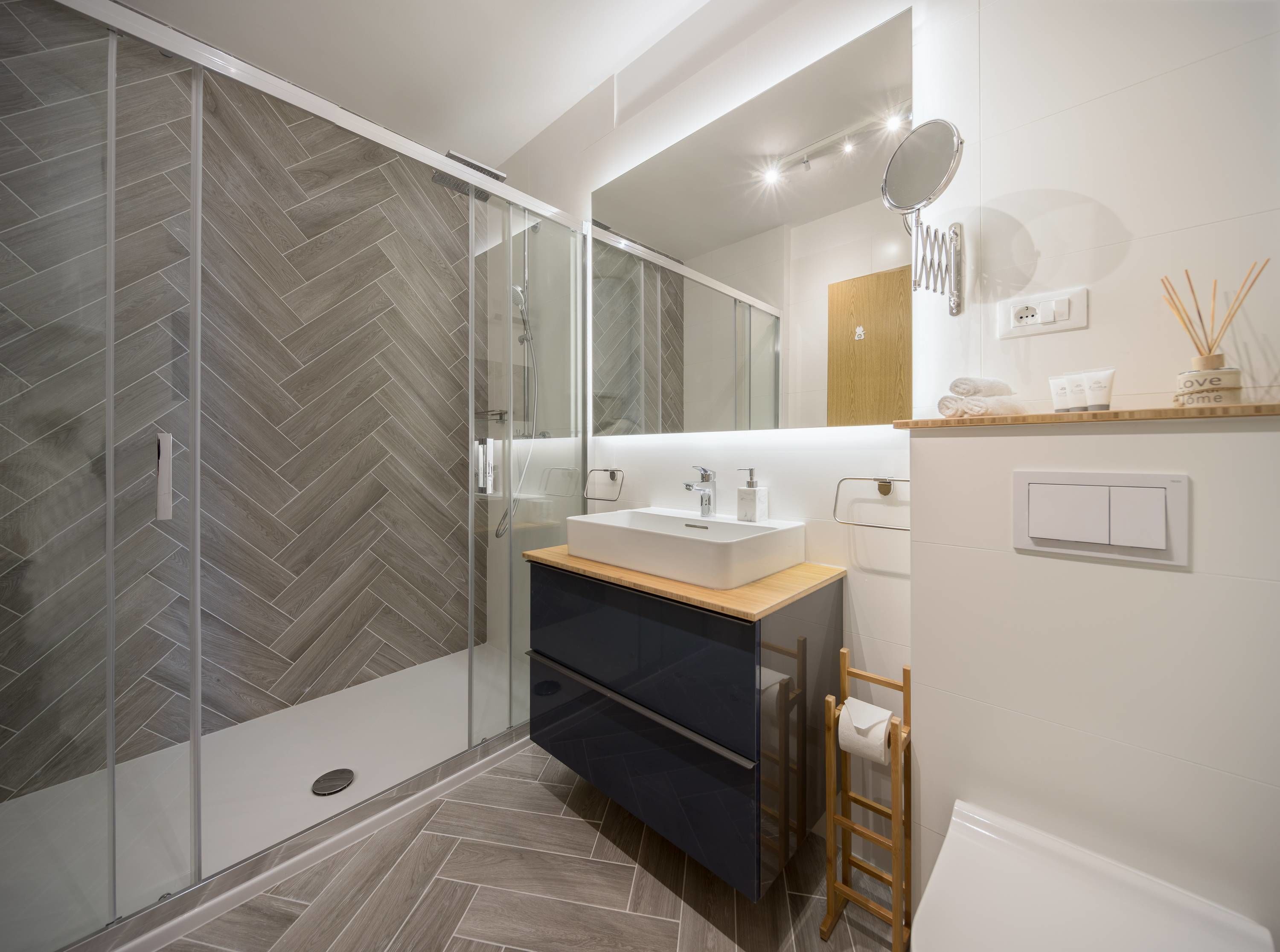 Un baño moderno con cabina de ducha de vidrio, un lavabo blanco y un mueble de tocador de madera.