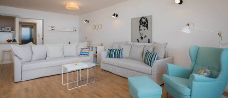 Un salon moderne avec un canapé blanc, un fauteuil bleu et une table basse. Des lampes murales et un tableau ornent le mur.