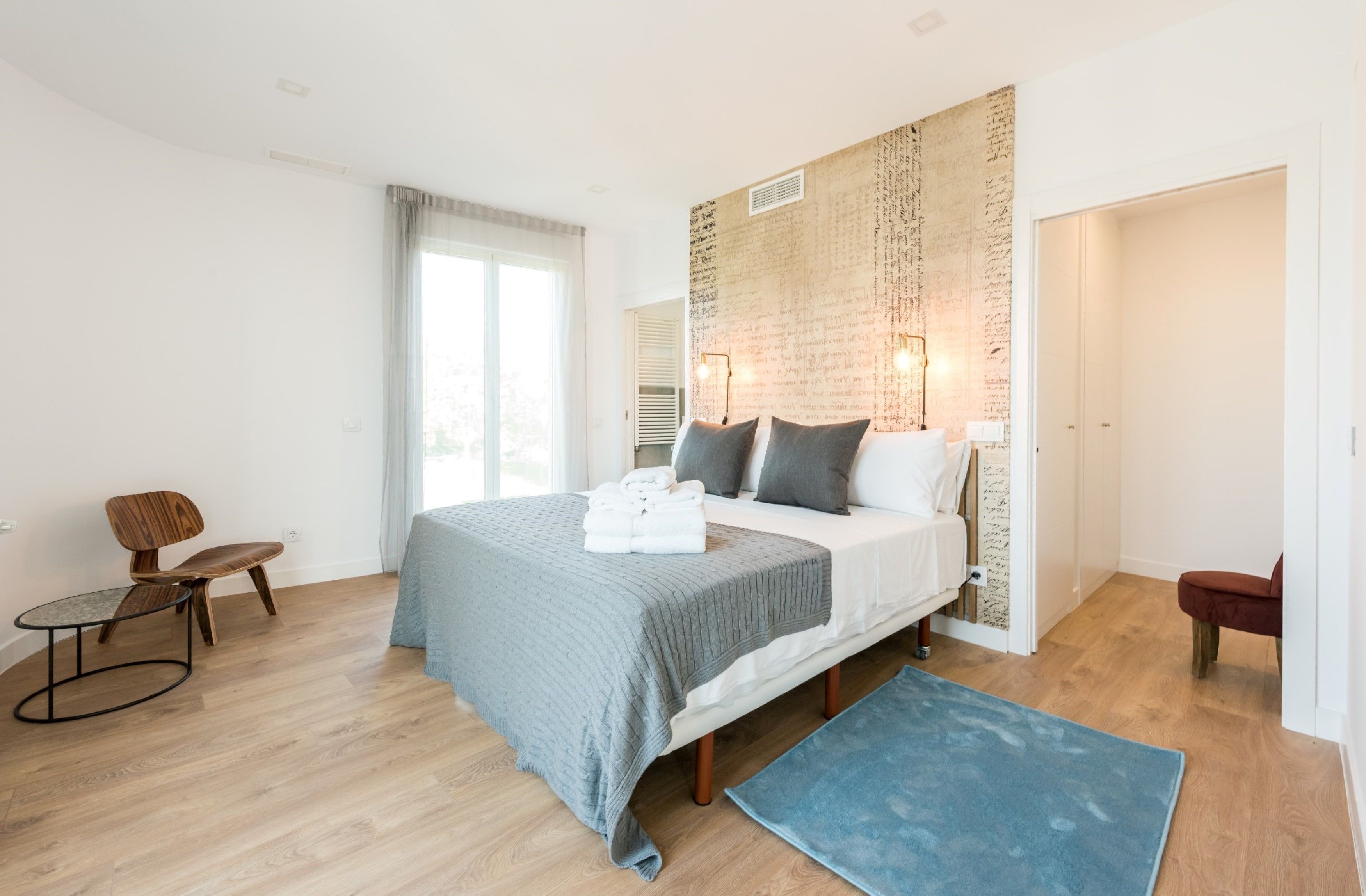 A modern bedroom with a large bed, a blue rug, a wooden chair, and a small table.
