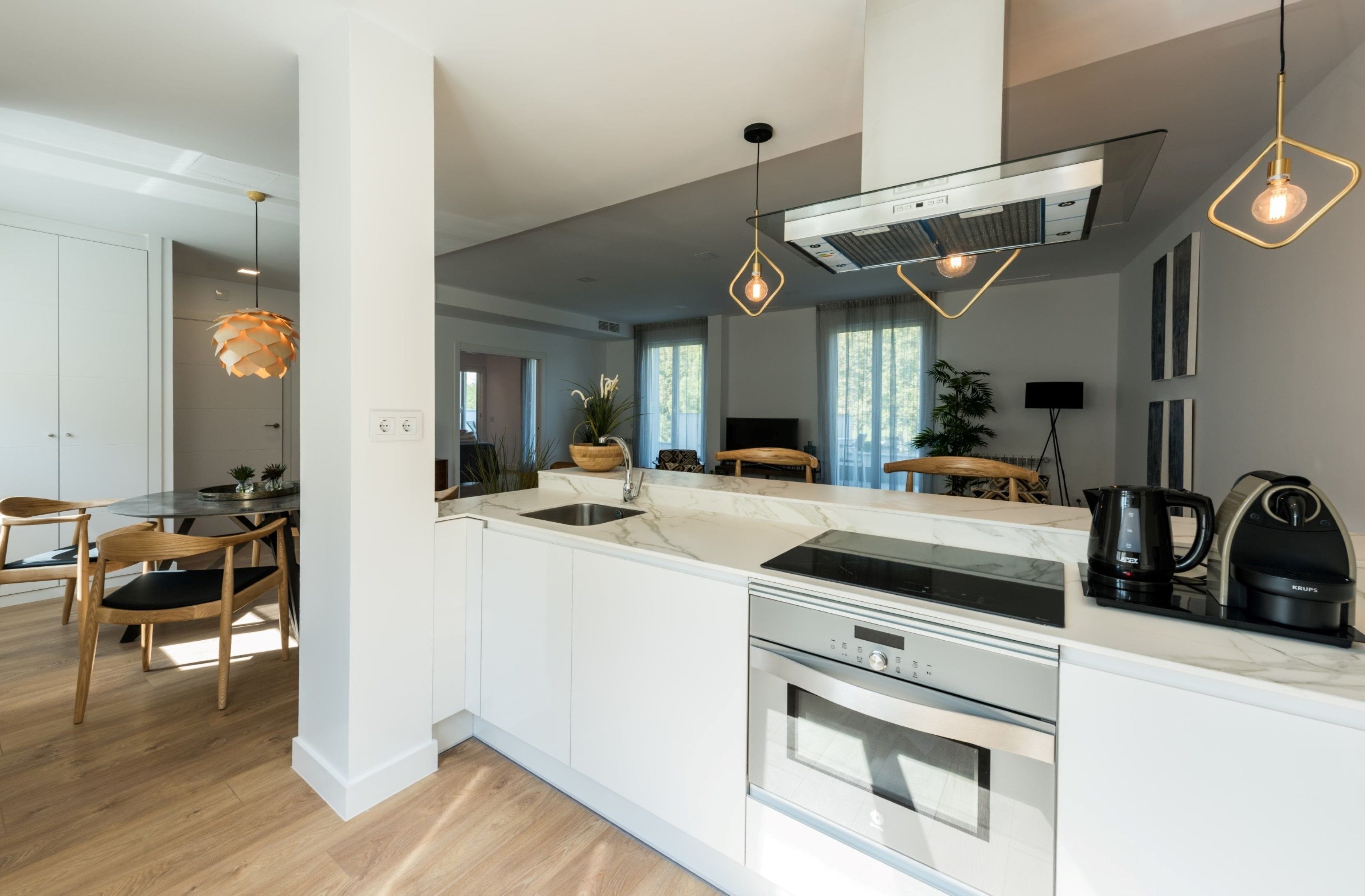 Una cucina moderna con mobili bianchi, elettrodomestici in acciaio inossidabile e illuminazione a sospensione.