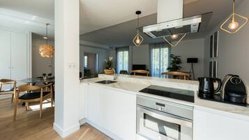 Una cucina moderna con mobili bianchi, elettrodomestici in acciaio inossidabile e illuminazione a sospensione.
