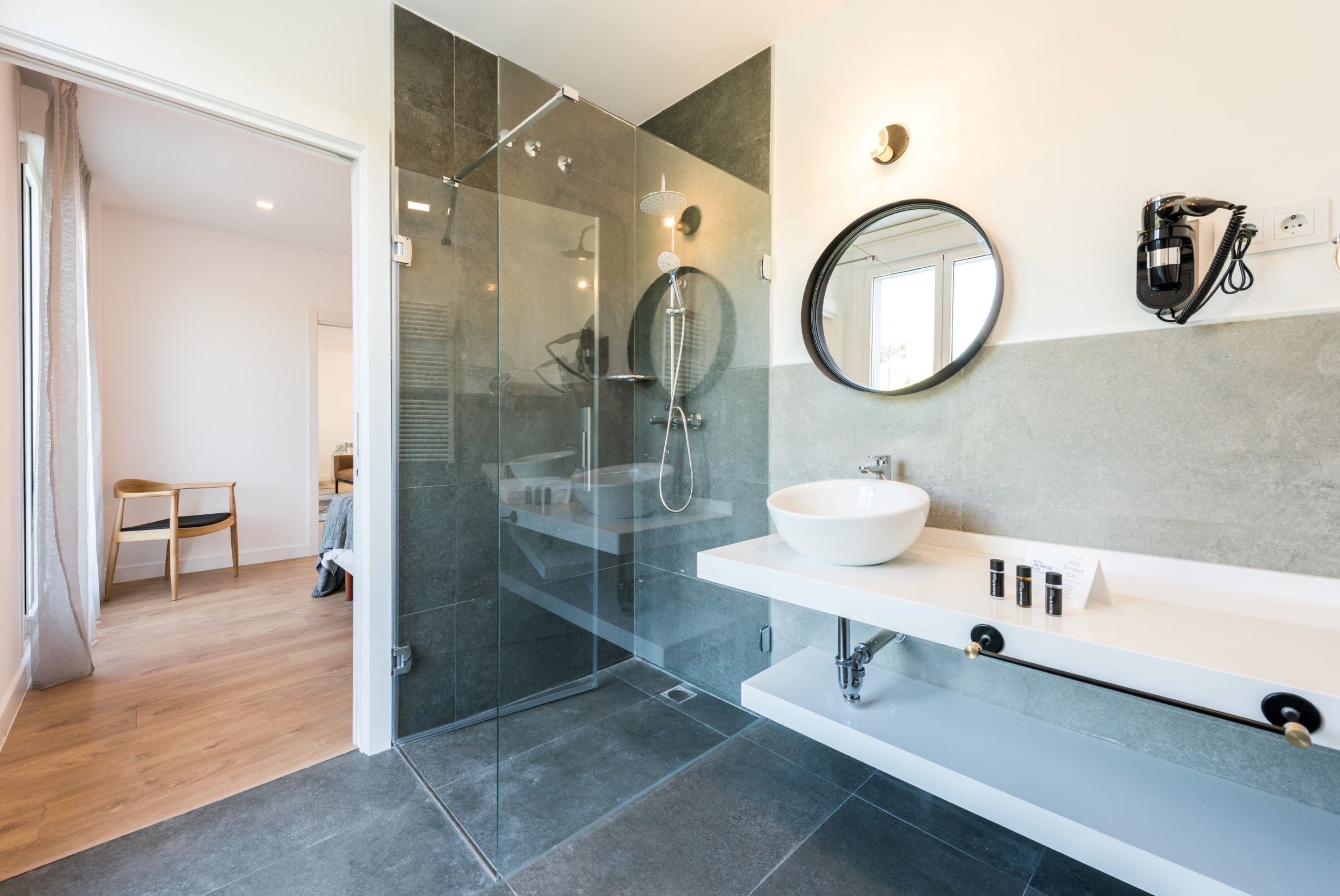 A modern bathroom with a glass-enclosed shower, a white sink, and a round mirror.