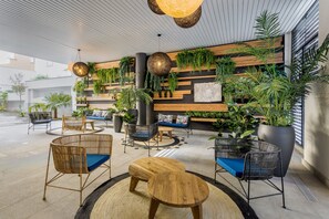 Un espacio interior moderno con asientos de madera y metal, rodeado de plantas verdes exuberantes y una gran planta en maceta.