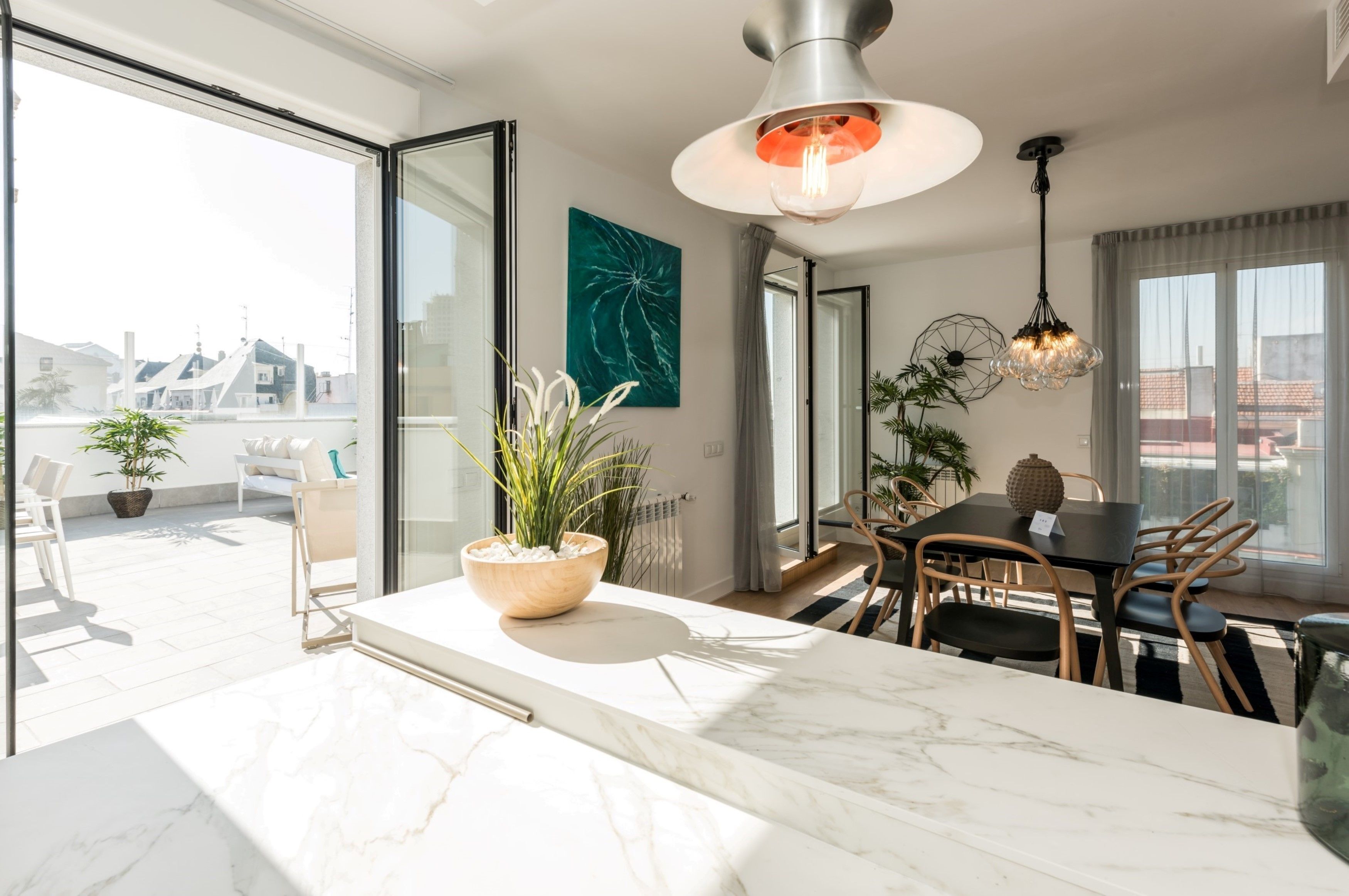 Una cocina moderna con encimera de mármol, una zona de comedor con mesa y sillas, y un amplio ventanal con vistas a edificios.