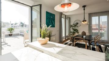 Una cocina moderna con encimera de mármol, una zona de comedor con mesa y sillas, y un amplio ventanal con vistas a edificios.