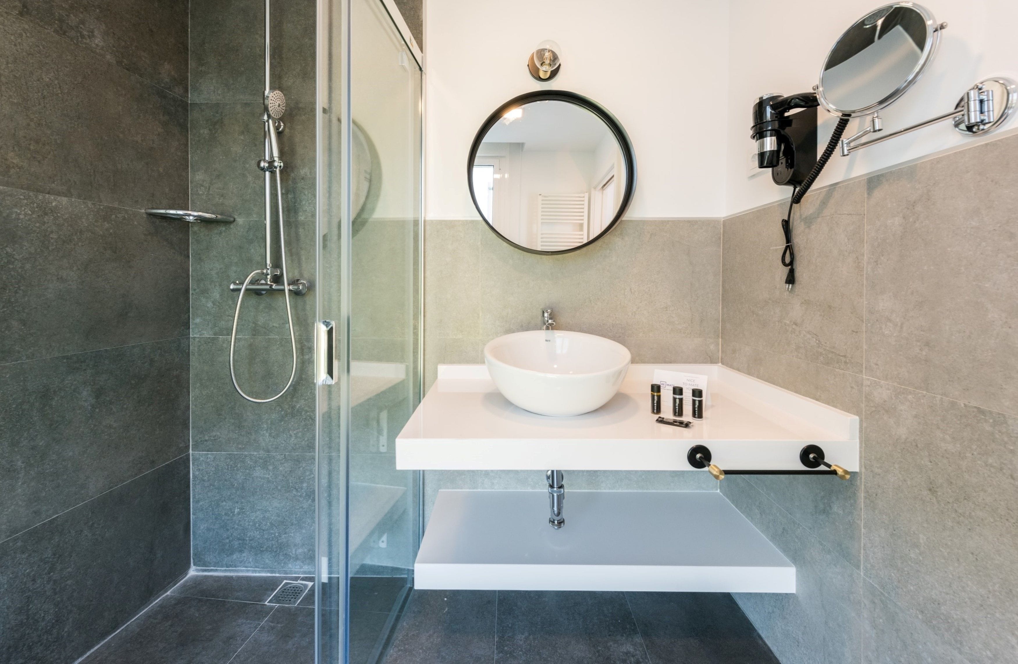 Une salle de bain moderne avec une douche à parois de verre, un lavabo blanc avec un miroir rond et un porte-serviettes.