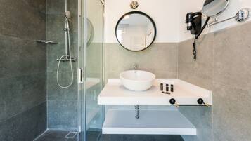 Une salle de bain moderne avec une douche à parois de verre, un lavabo blanc avec un miroir rond et un porte-serviettes.