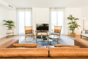 Un salon moderne comprenant un canapé, deux fauteuils, une table basse et un téléviseur.