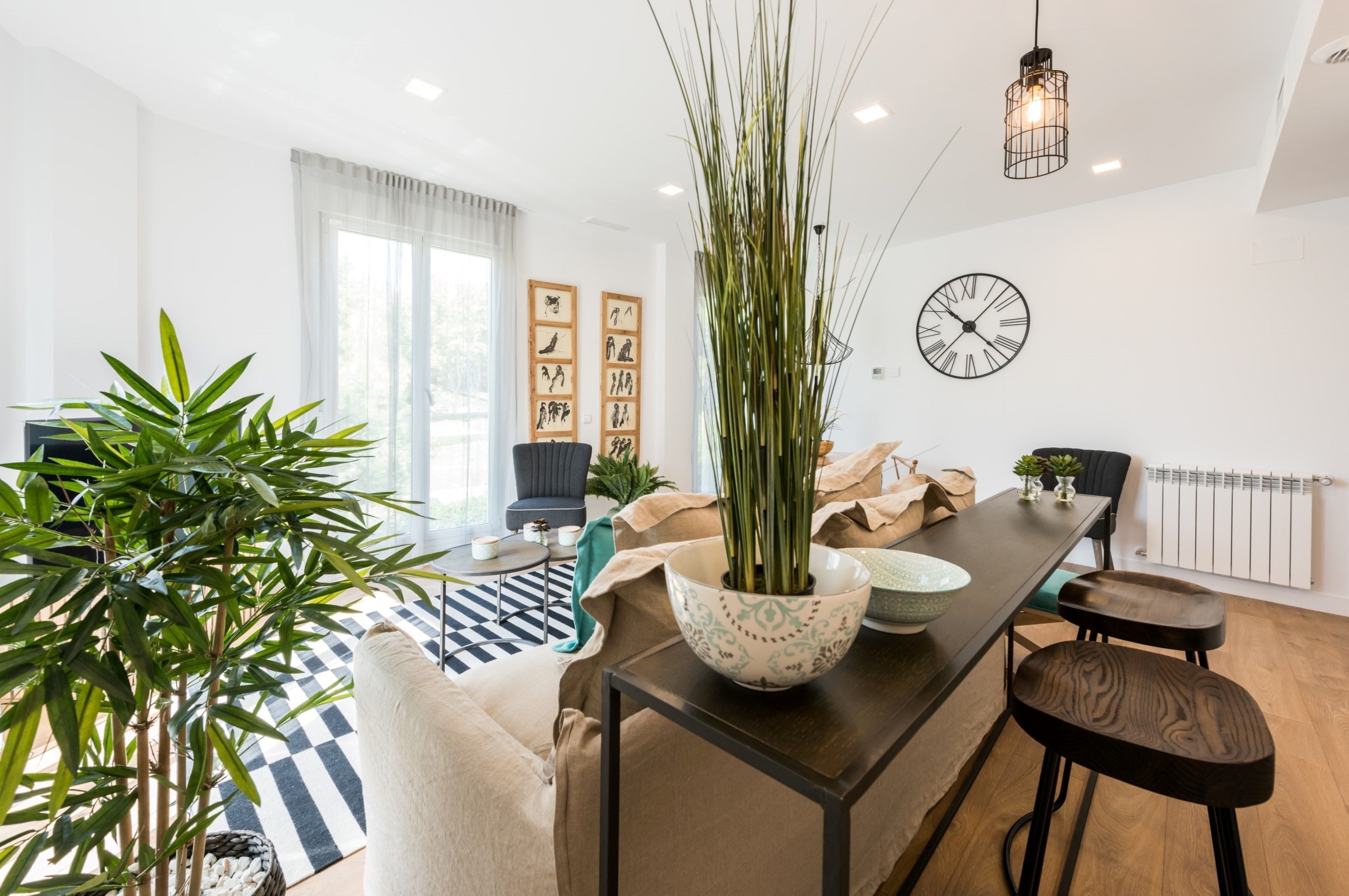 Een moderne woonkamer met een eethoek, met een grote plant, een klok en een minimalistisch design.