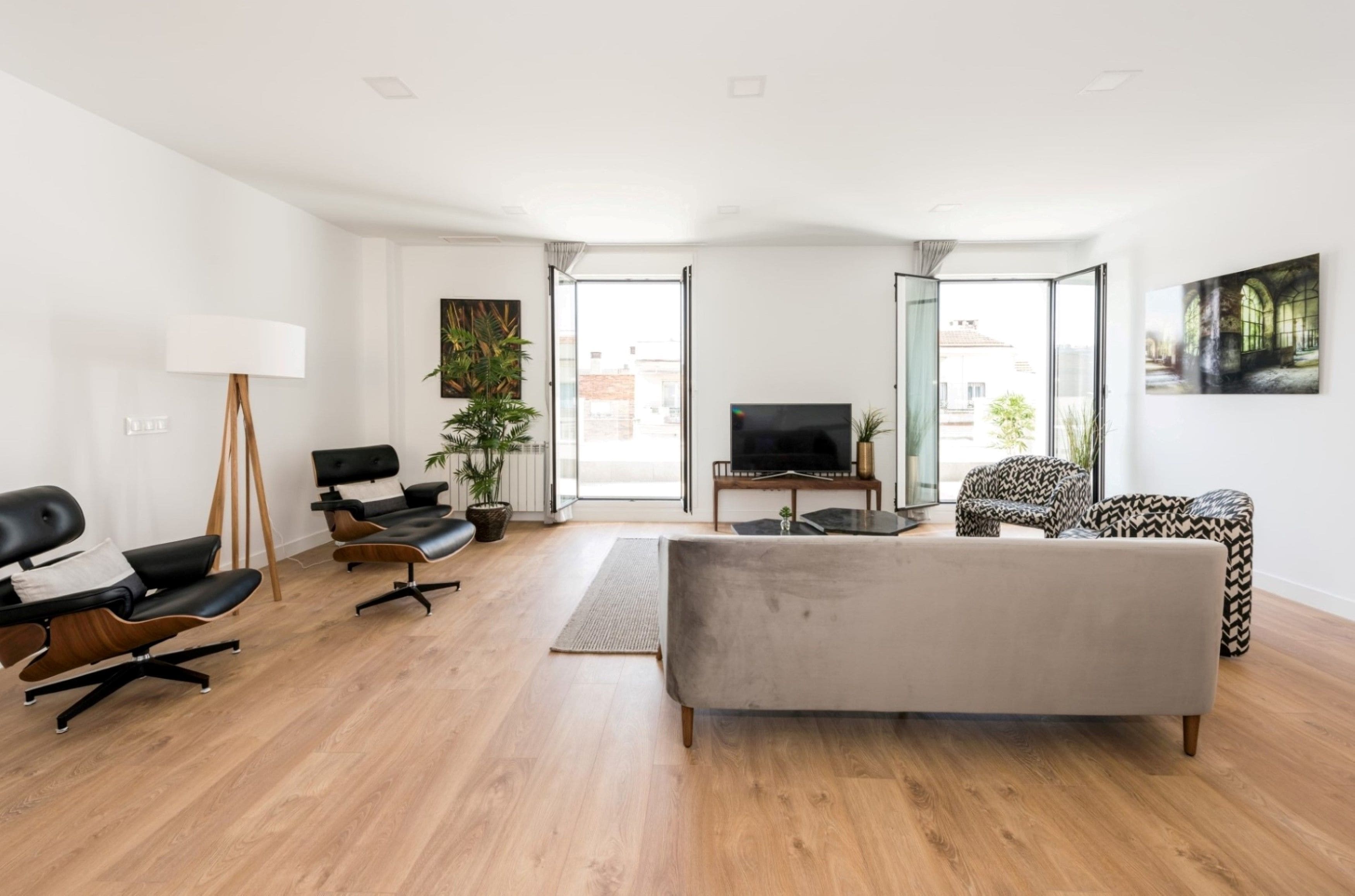 A modern living room with a grey sofa, two black leather chairs, a floor lamp, and a TV.