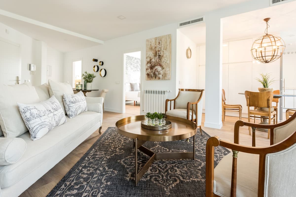 Una sala de estar moderna con un sofá blanco, una mesa de centro redonda y un comedor con sillas de madera.