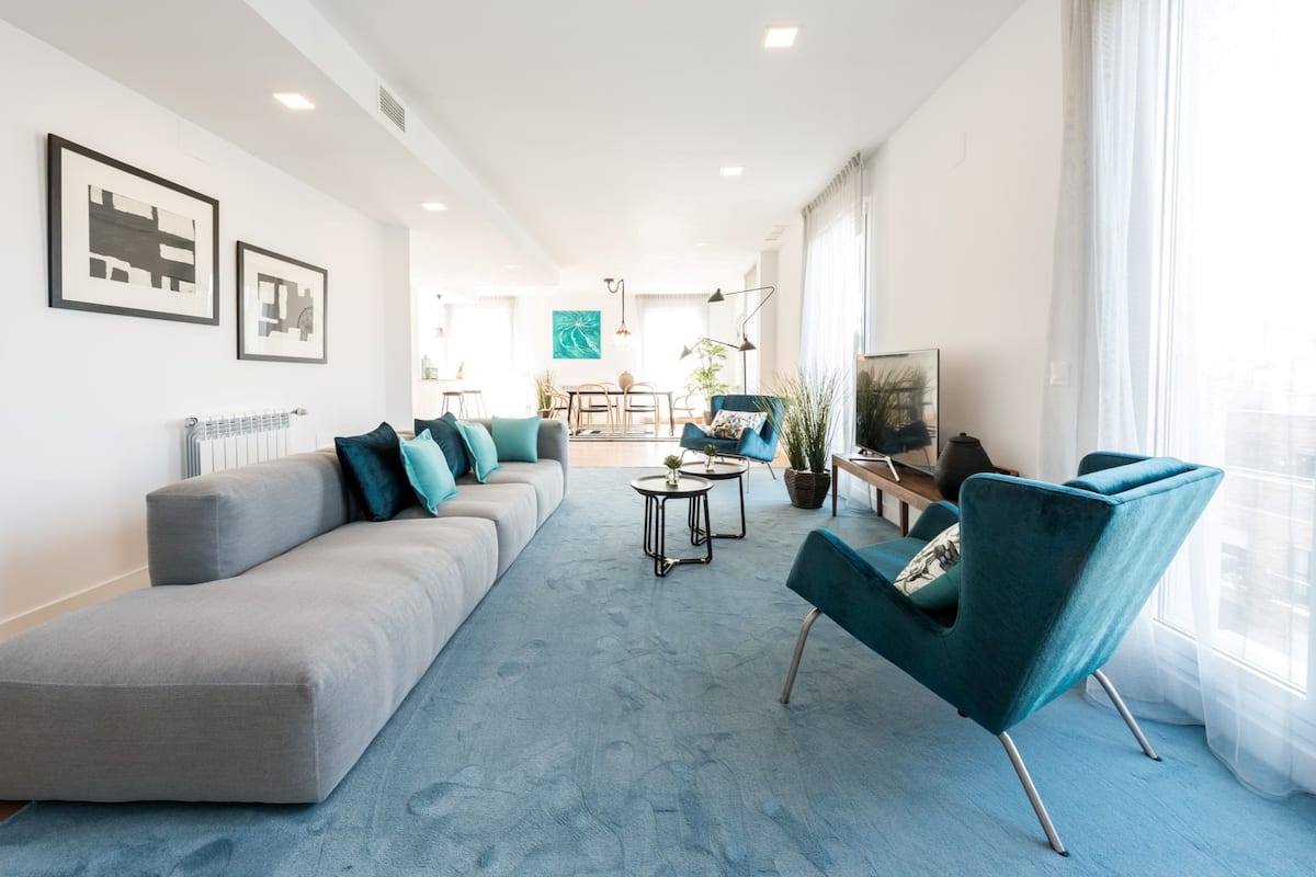 Una sala de estar moderna con un sofá gris, sillones color turquesa y una mesa de centro.