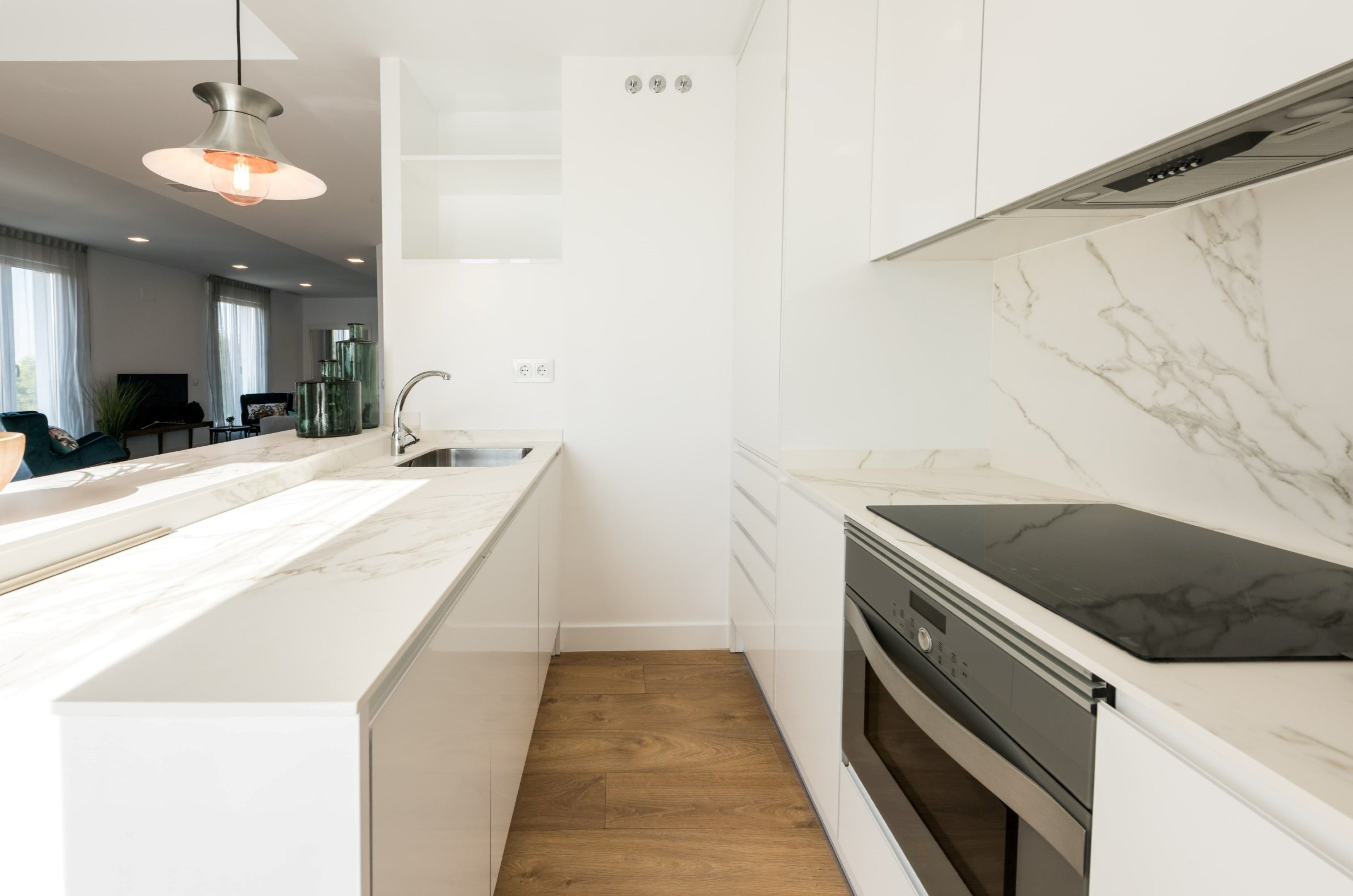 A modern kitchen with white cabinetry, a marble countertop, a black induction cooktop, and a wooden floor.