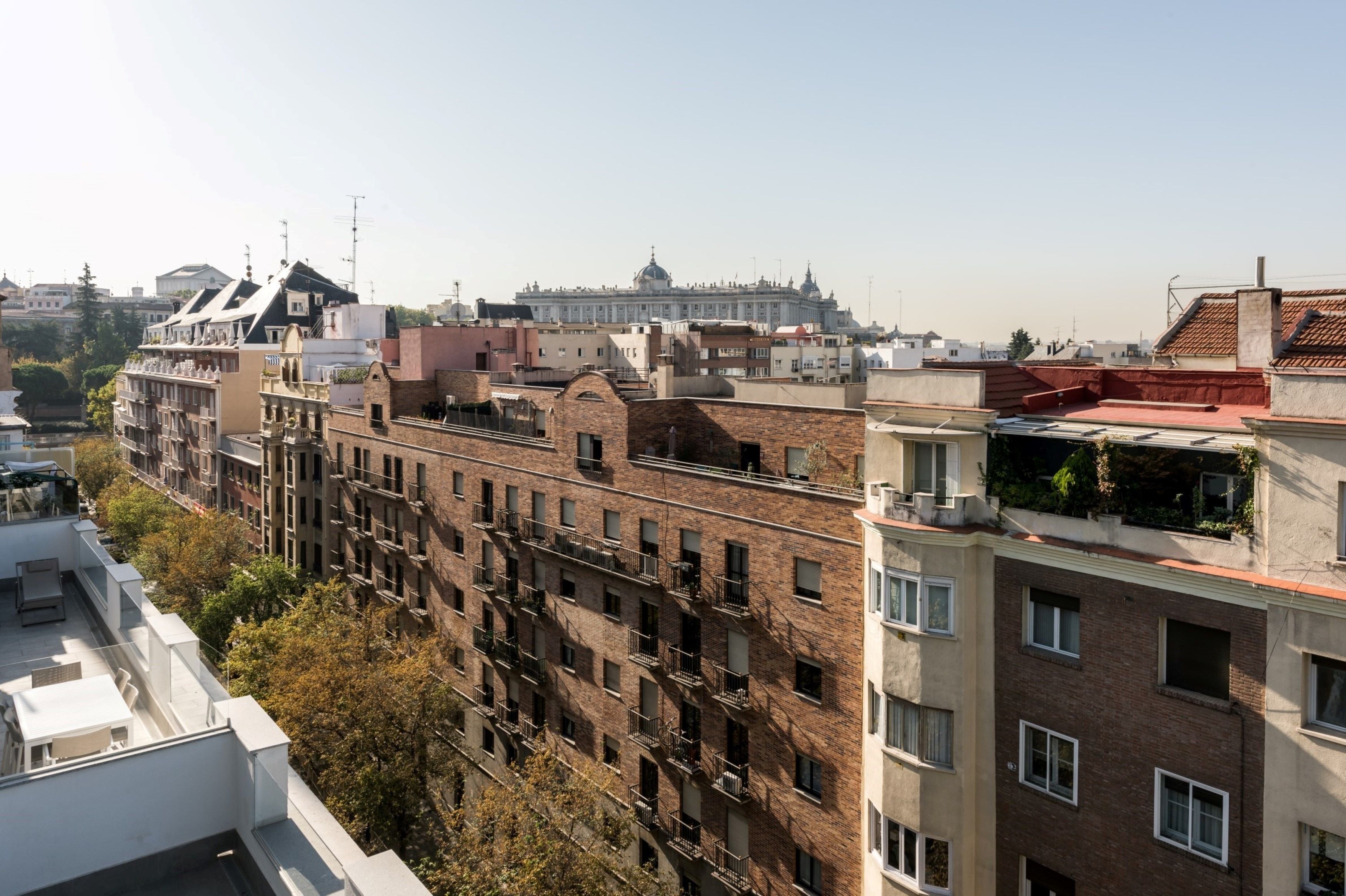 A multi-story building with a brick facade, multiple balconies, and a clear view of a large, historic building in the background.