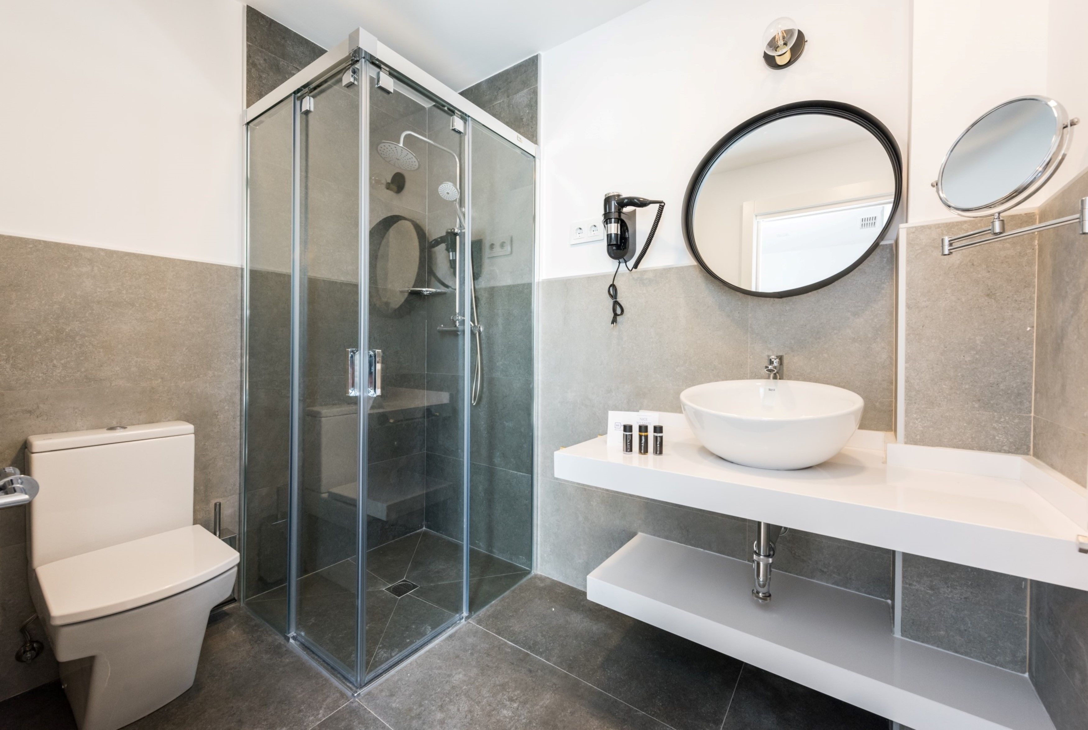 Un baño moderno con ducha envuelta en vidrio, un lavabo blanco y dos espejos fijos a la pared.