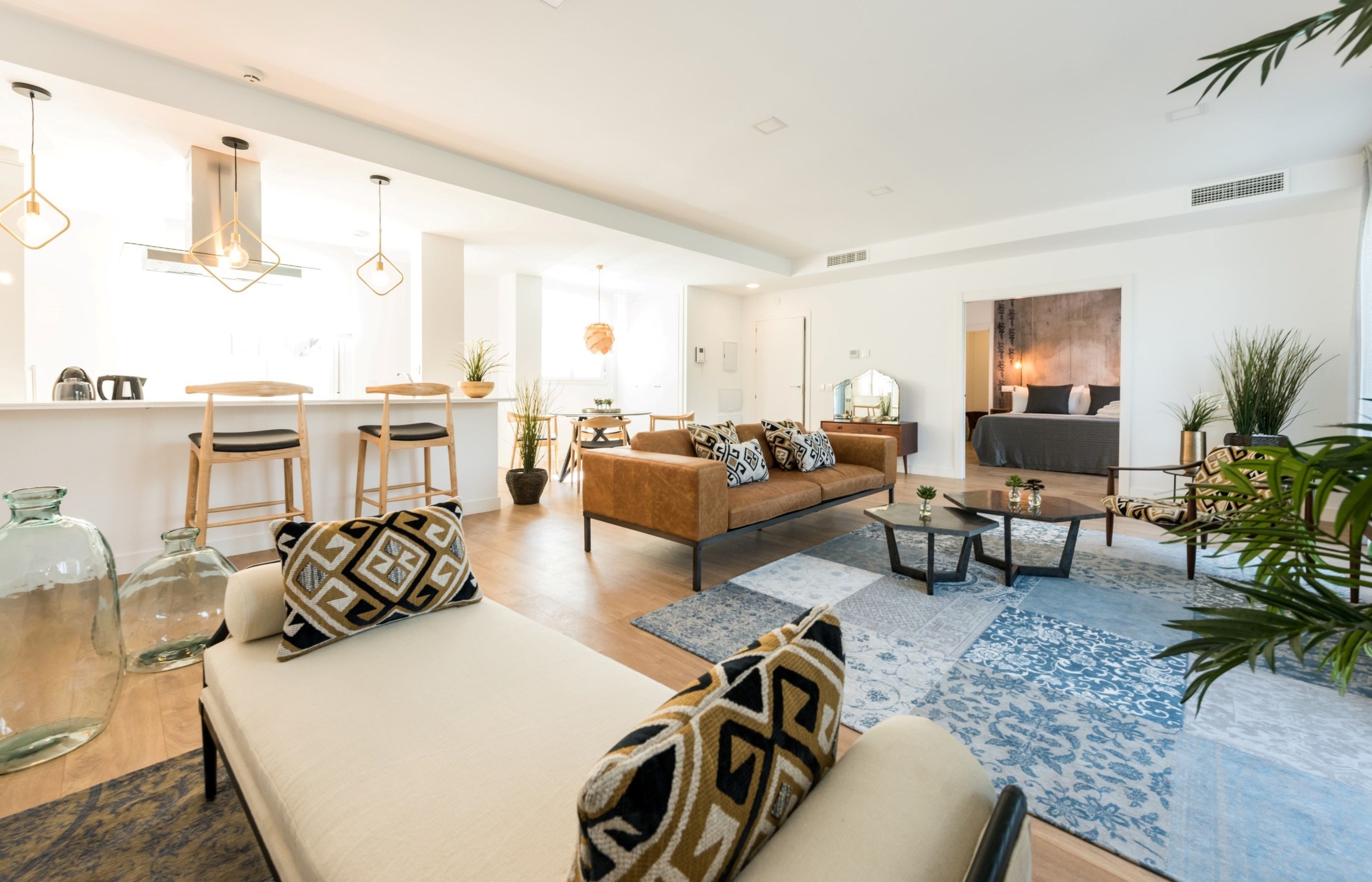 A modern living room with a sofa, coffee table, and chairs. There is a kitchen area with a kettle and a dining table.