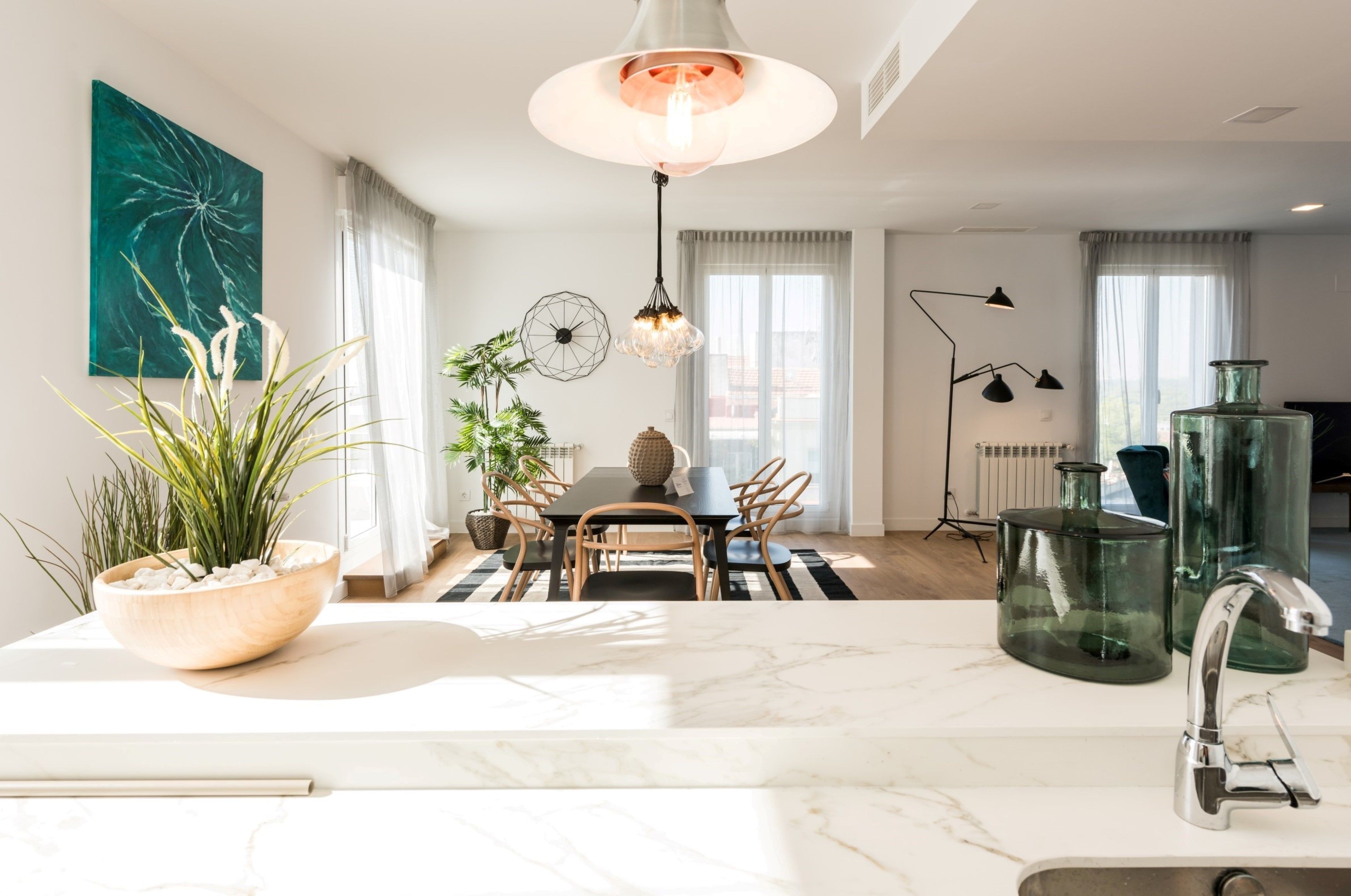 Una cocina moderna con encimera de mármol, un comedor con mesa y sillas, y un ventanal con cortinas.