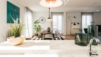 Una cocina moderna con encimera de mármol, un comedor con mesa y sillas, y un ventanal con cortinas.