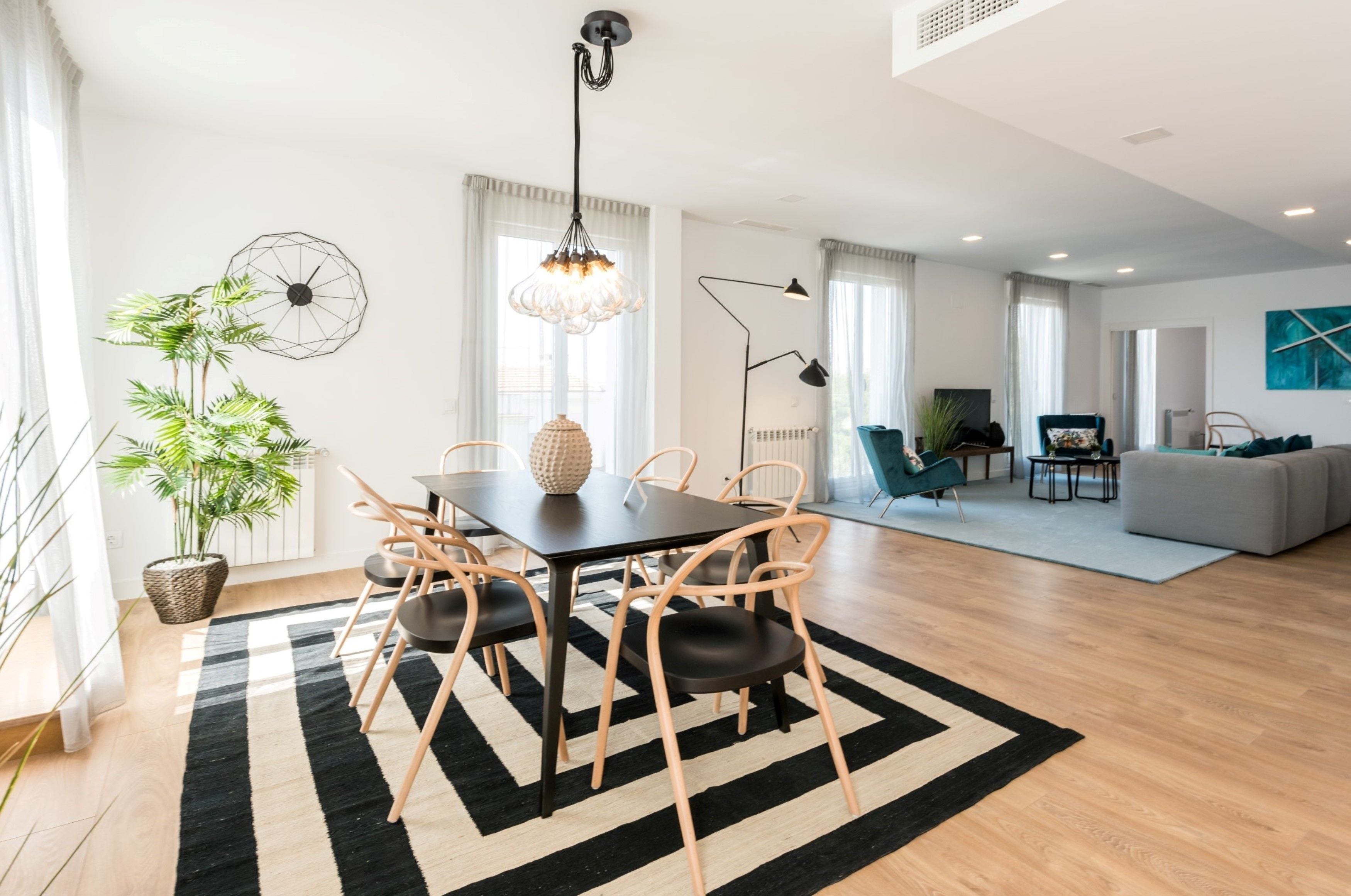 Una sala de estar moderna con comedor, que incluye un tapete blanco y negro, muebles de madera y una planta grande en maceta.