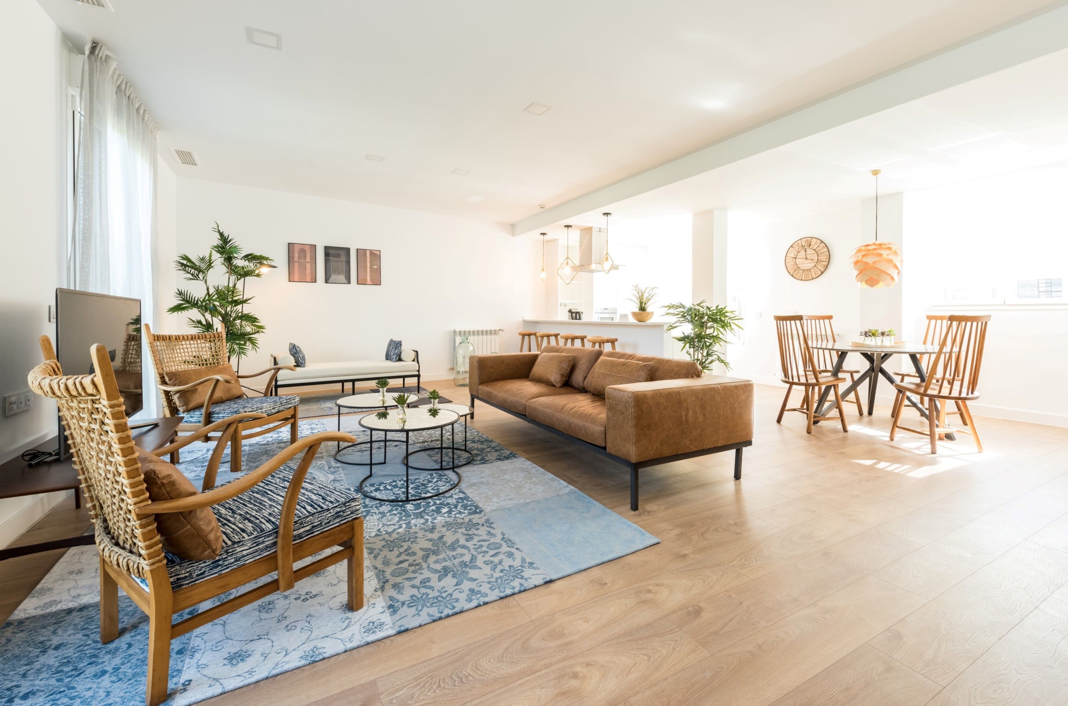 Un salon moderne avec un canapé, une table basse et des fauteuils. On y trouve également un coin repas avec une table et des chaises. La pièce est dotée d’un parquet et de murs blancs.