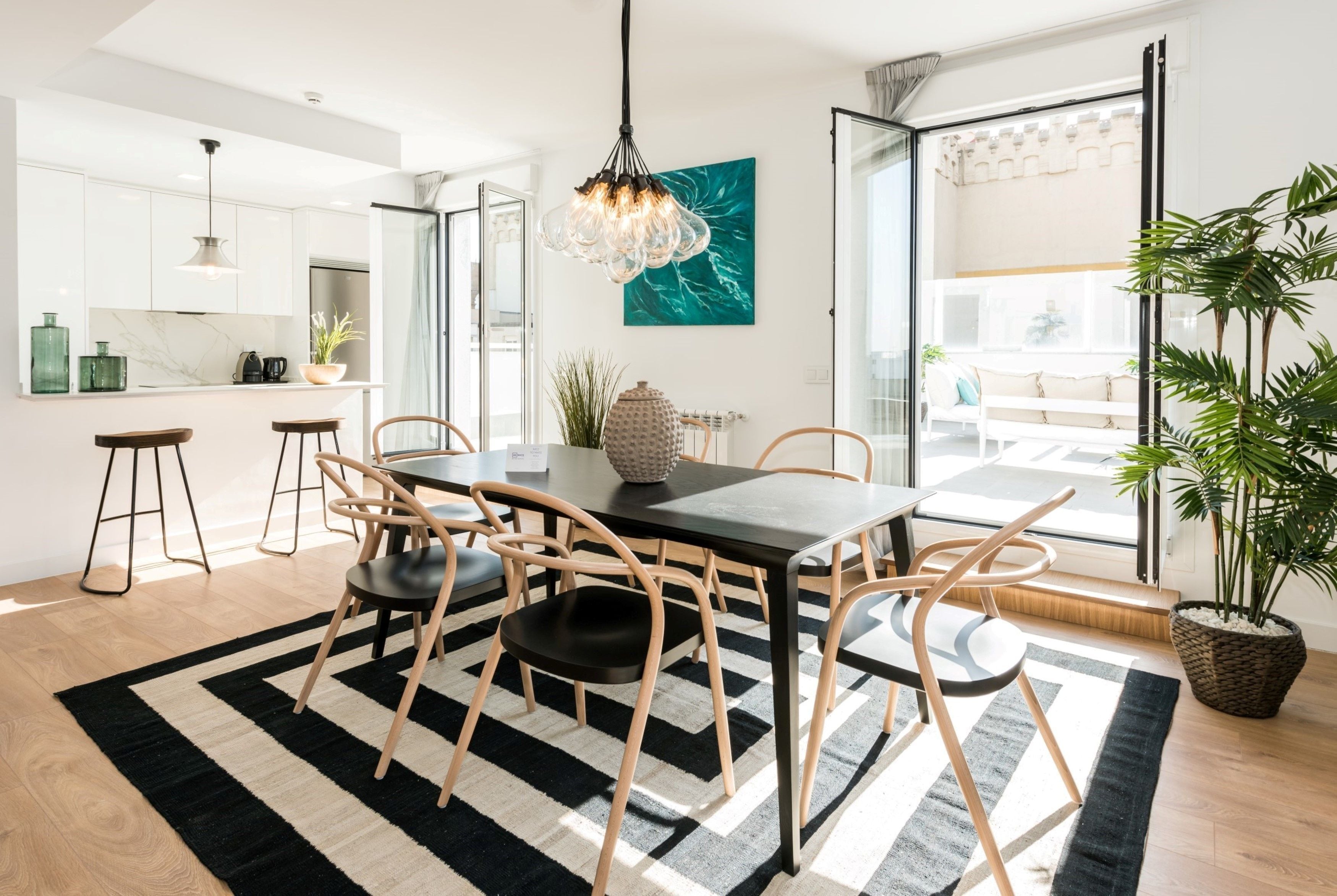 Una cocina moderna con armarios blancos, una mesa de comedor negra y sillas de madera. Hay un ventanal con vistas al exterior.