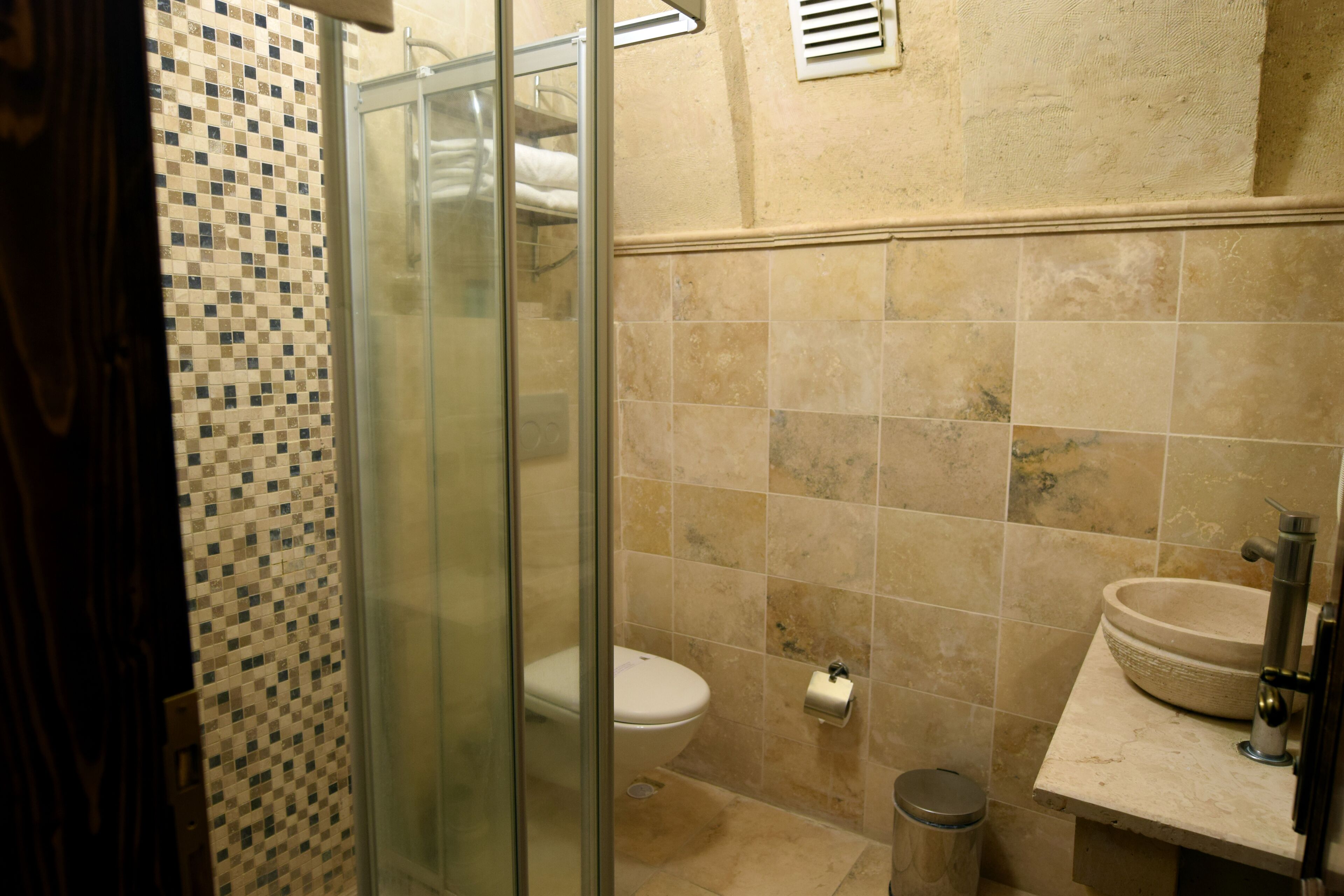 A bathroom with a glass shower enclosure, a toilet, a sink, and tiled walls.