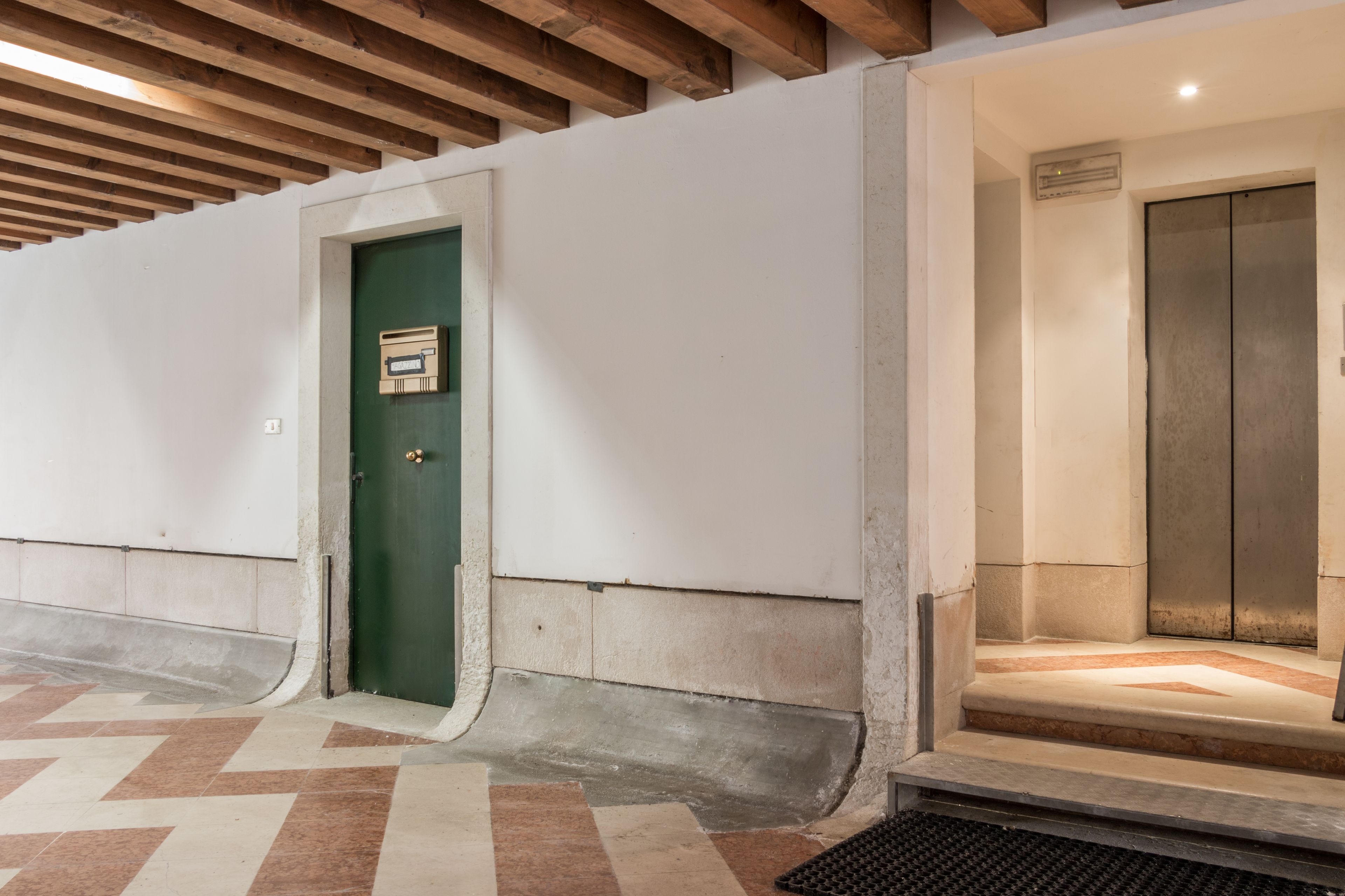 Un couloir avec une porte verte, un sol carrelé et un ascenseur.