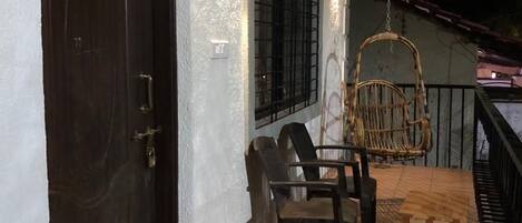 A balcony with a wooden table and chairs, a hanging chair, and a dark door.