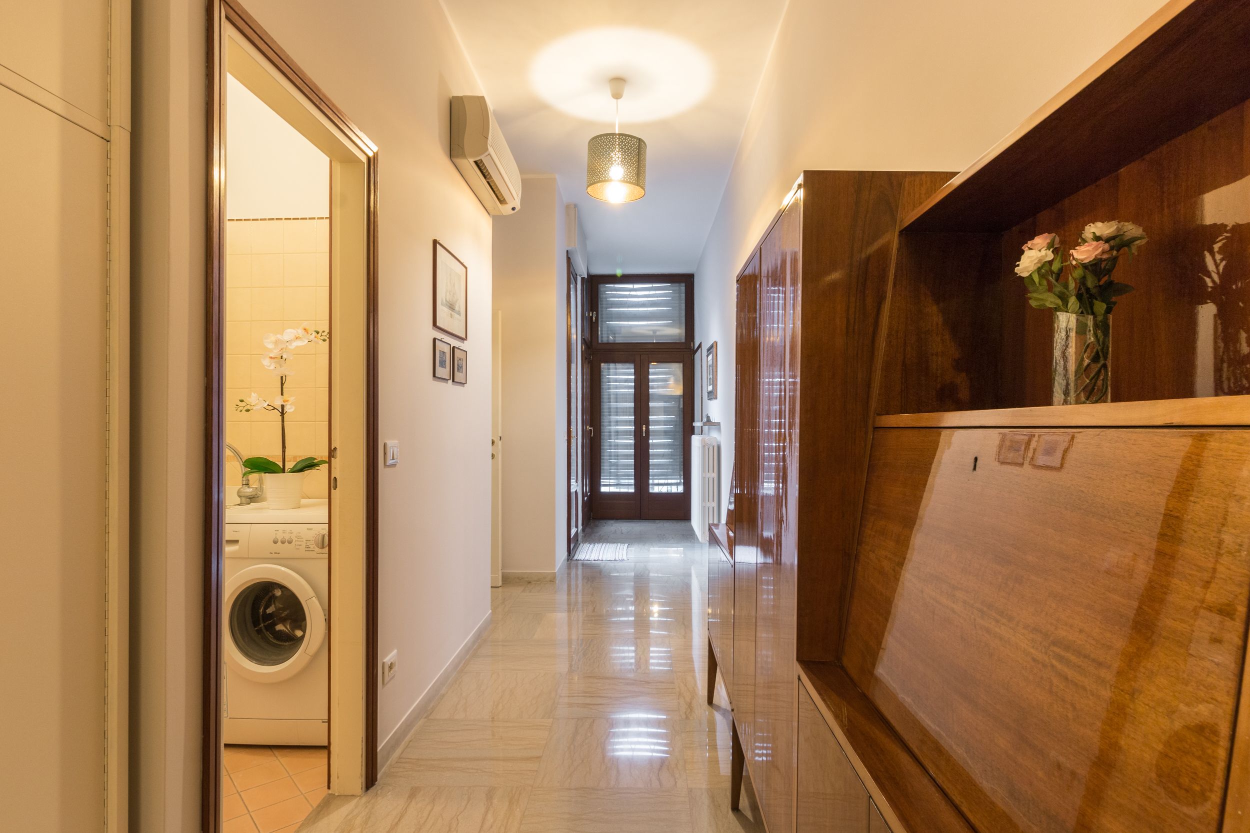 A hallway with a washing machine, a wooden cabinet, and a vase with flowers.