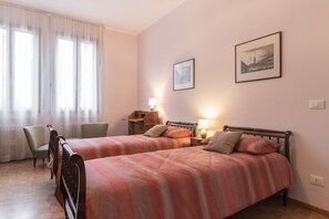 A room with two beds, a desk, a chair, and two framed pictures on the wall.
