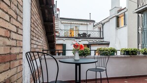 A terrace with two black metal chairs and a small round table, a white vase with flowers, and a brick wall. - Rialto Bridge Venetian Style (Venice)