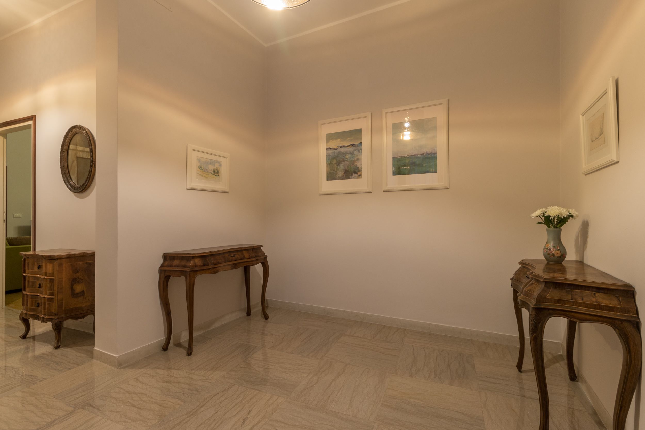 A hallway with wooden furniture, framed pictures on the walls, and a marble floor.