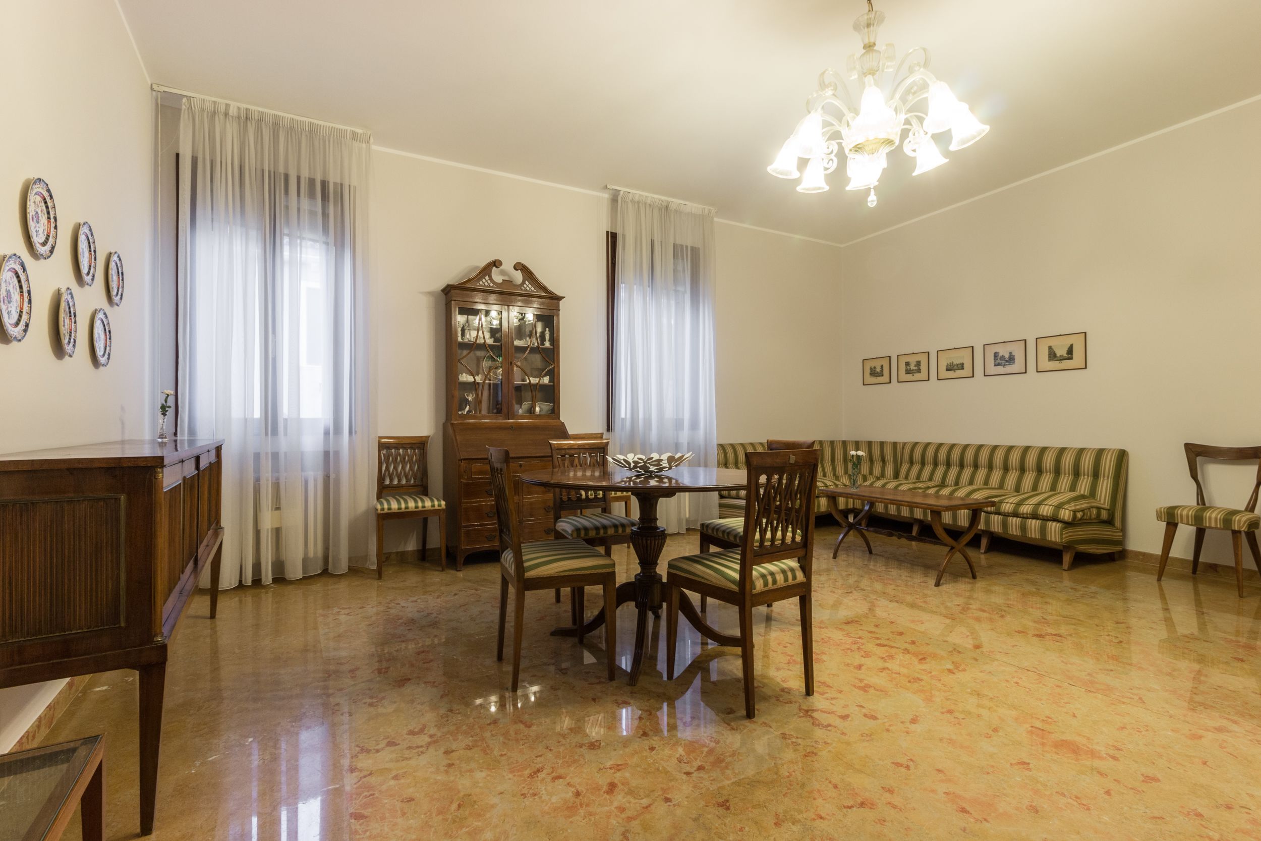 A dining area with a round table, chairs, a wooden cabinet, and a striped sofa.