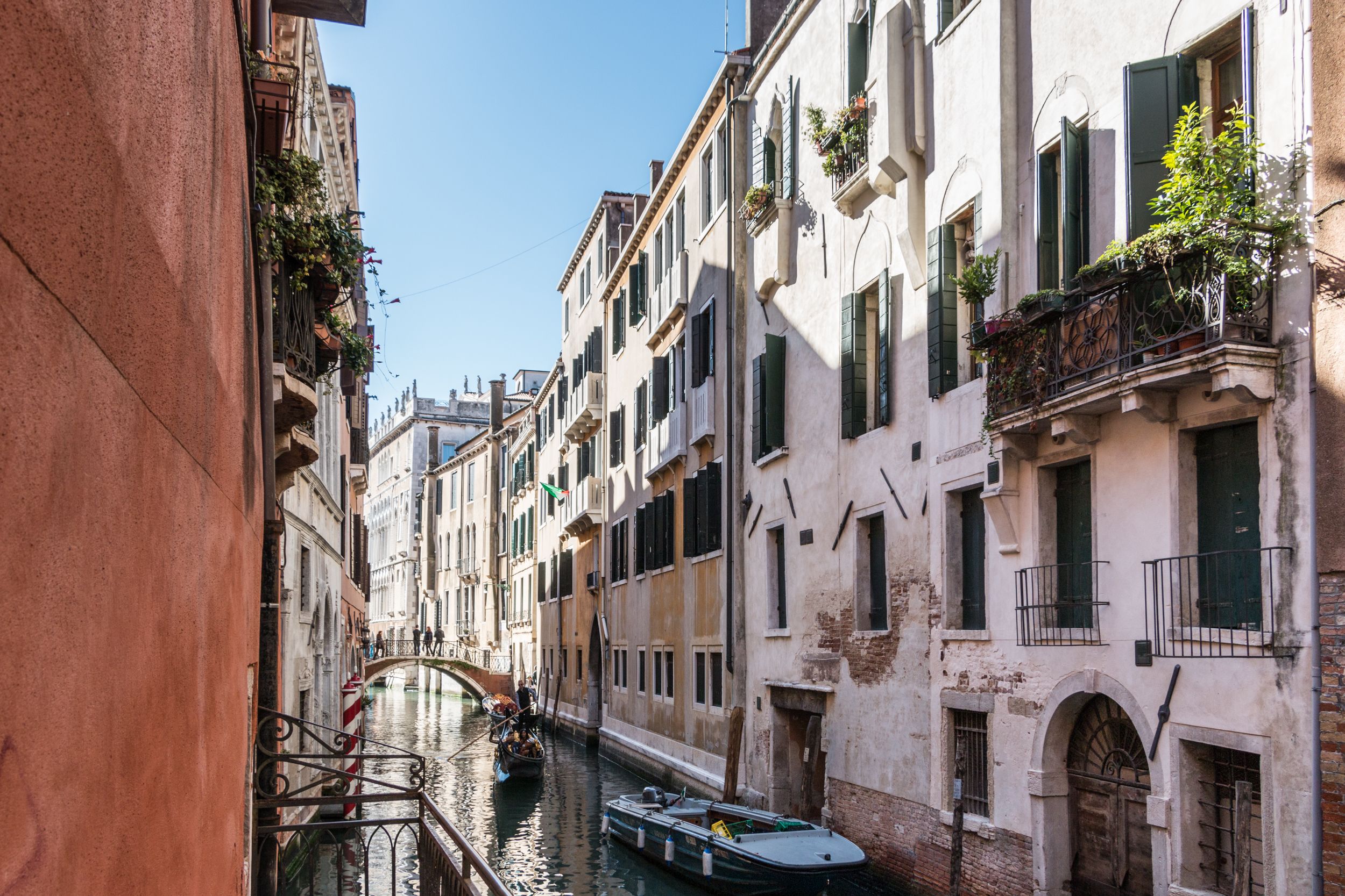 Un canal étroit à Venise, bordé de bâtiments traditionnels de chaque côté, avec une gondole et un pont visible au loin.