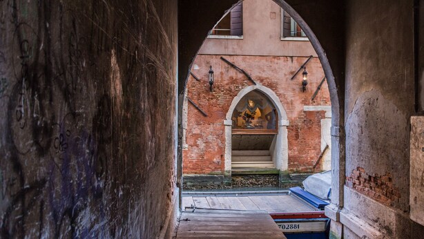 An arched passageway with a rustic brick wall, a wooden bench, and a small table with a sign. - Rialto Bridge Venetian Style (Venice)